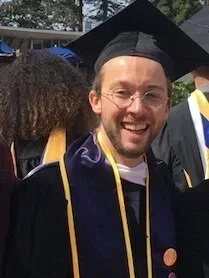 A man wearing graduation cap and gown, smiling at a ceremony.