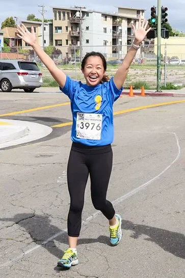 A woman in athletic clothing celebrating with arms raised in a parking lot during a race event.