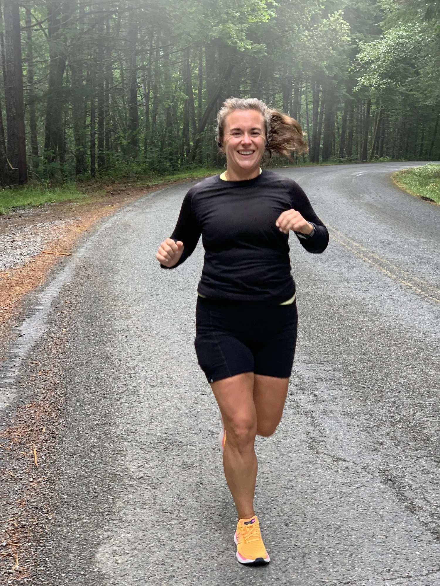 A woman running along a curving forest trail with tall trees and green foliage.