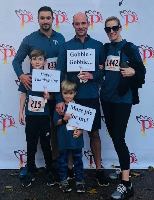 Family of four at a Thanksgiving run, holding humorous signs about turkey and pie.