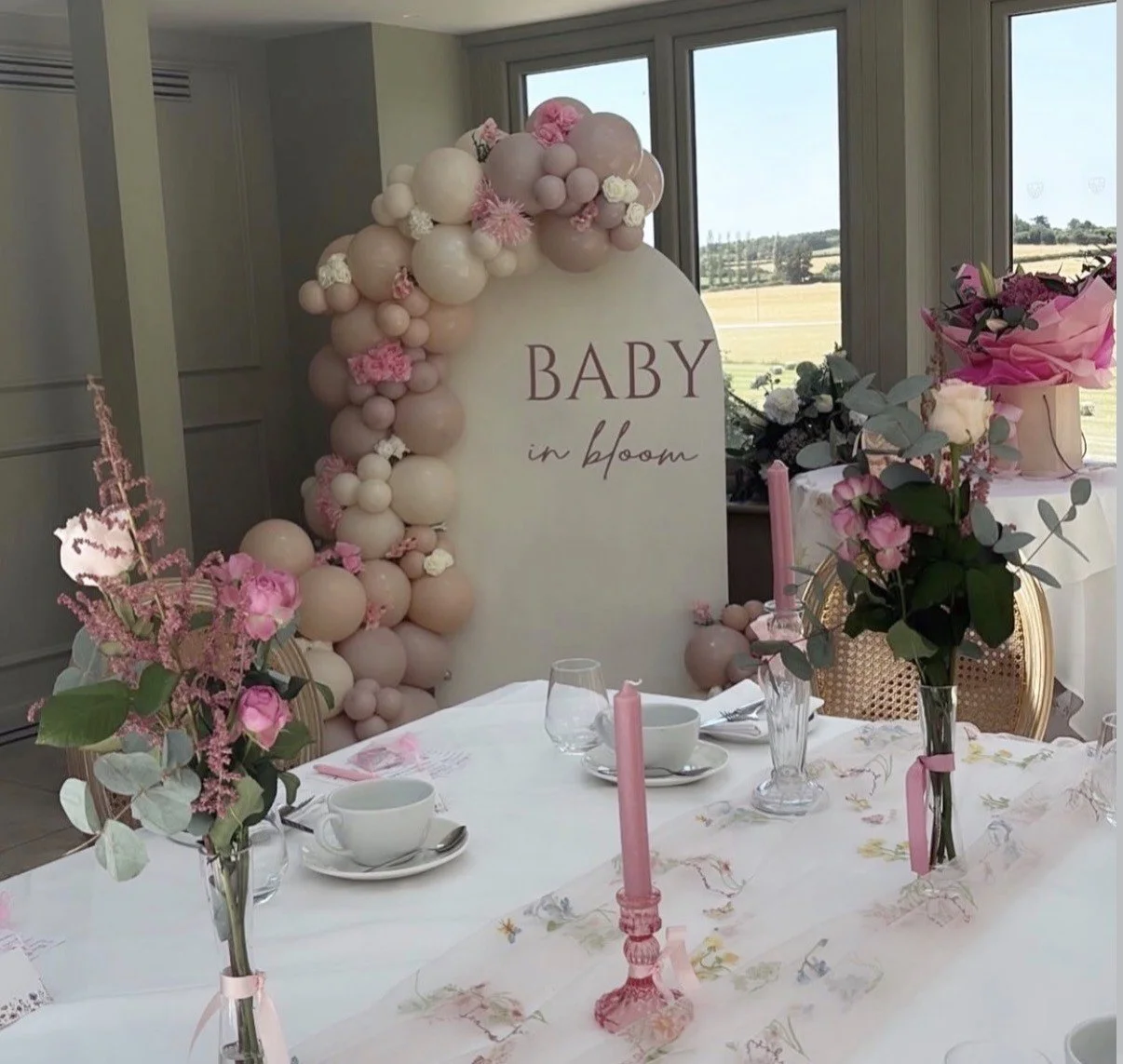 Baby shower table decorated with pink and white flowers, candles, and a sign reading 'Baby in bloom' with balloon arrangements.