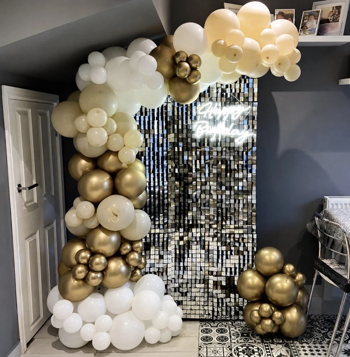 Decorative balloon arrangement in white and gold, with a shimmering backdrop and a neon sign that reads 'Happy Birthday,' for a birthday celebration.