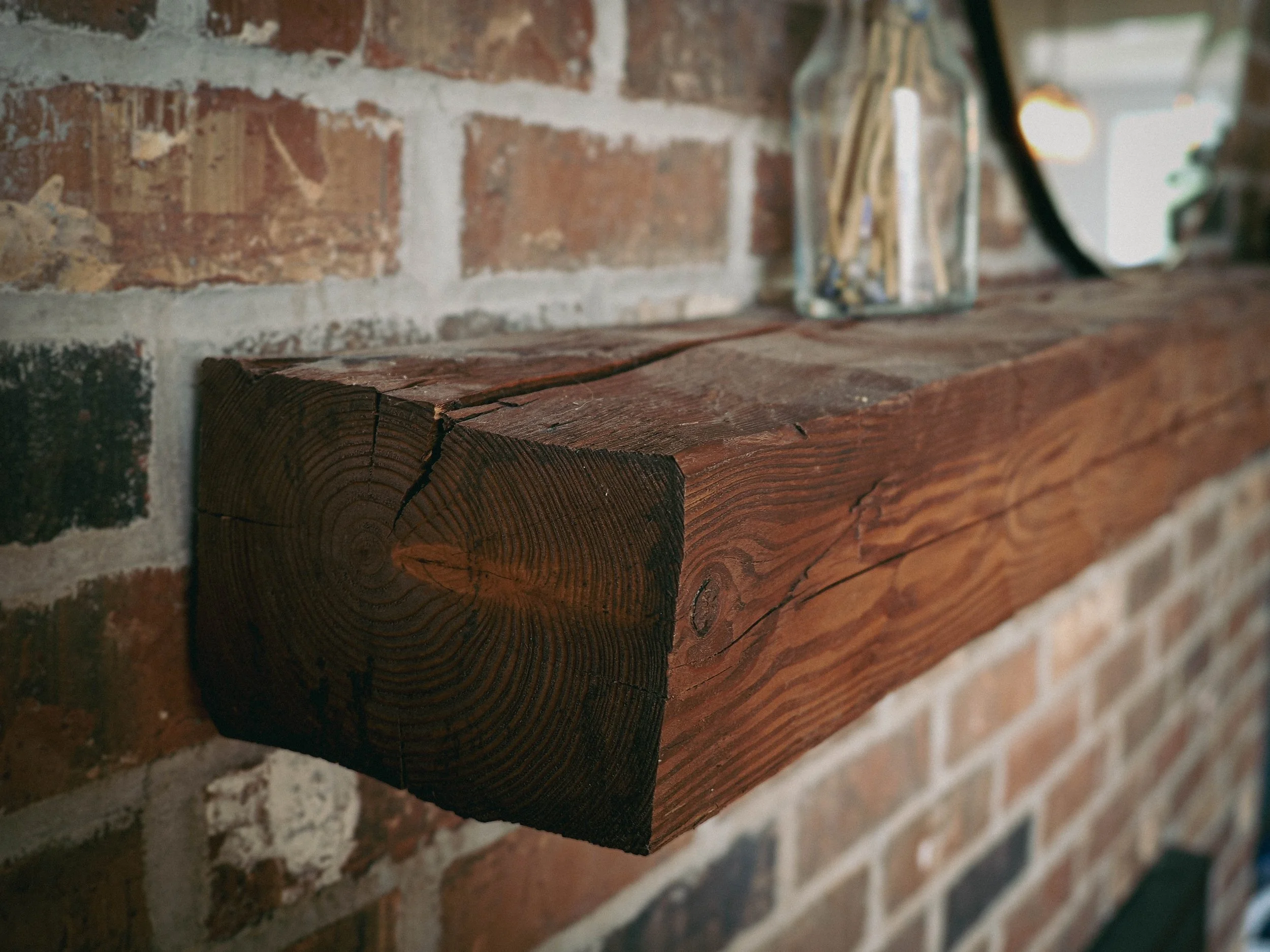 A solid reclaimed timber mantel, chosen to complement the character of the home's original exposed brick. The natural checking, grain, and weathered finish preserve the wood's history while adding warmth to the space.