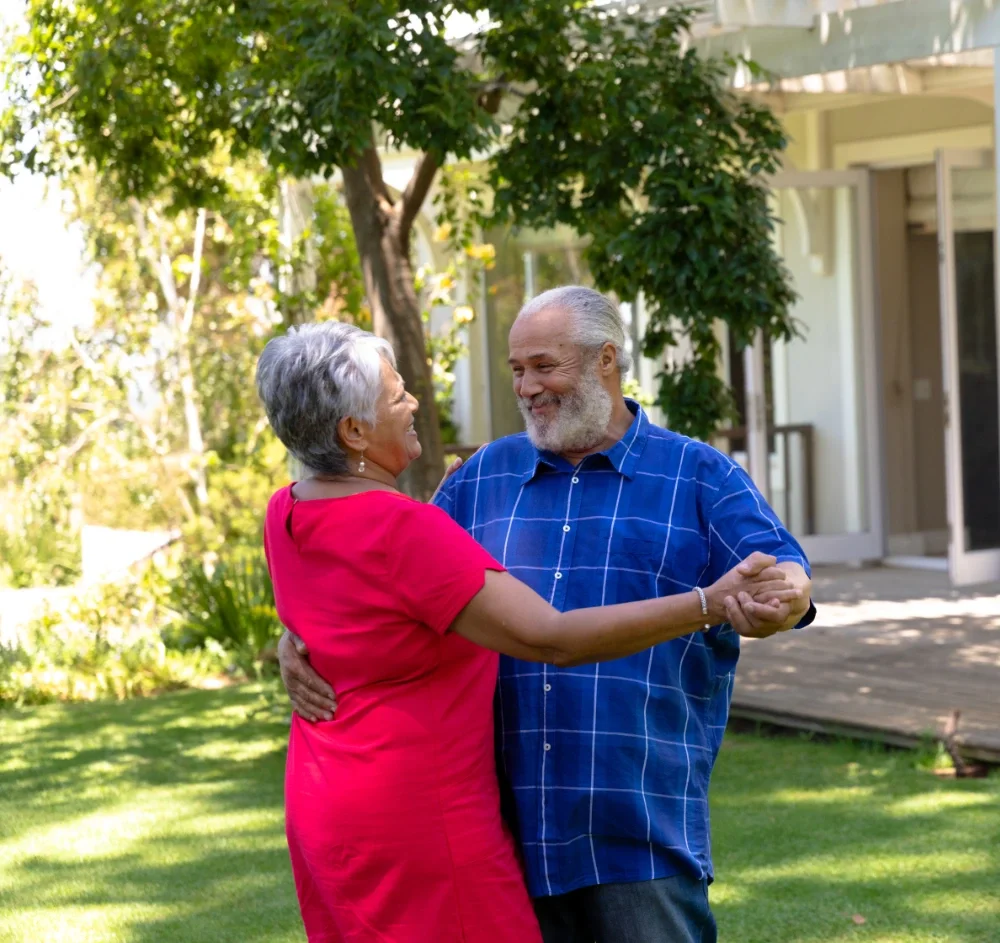 An elderly couple is dancing outdoors in a garden