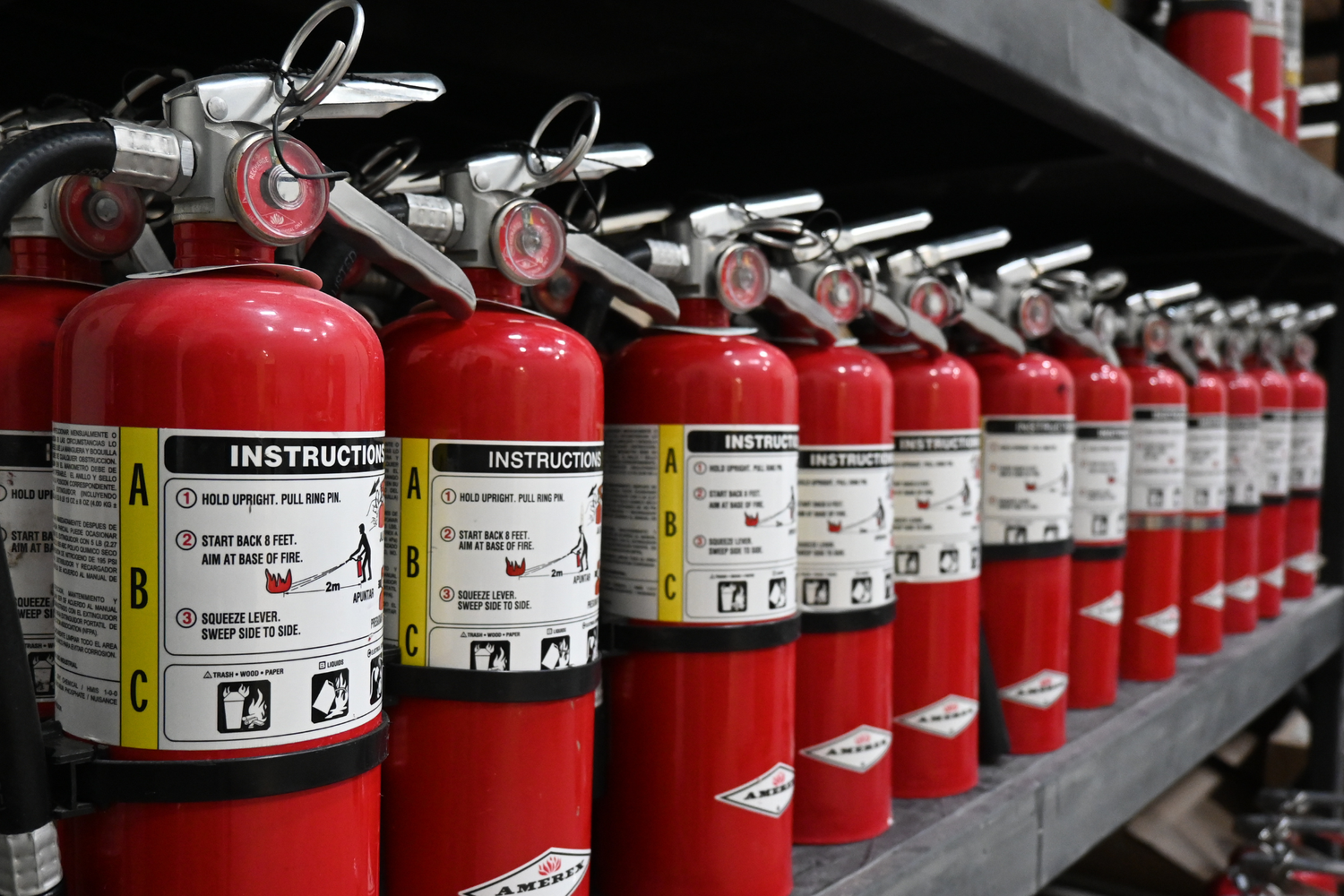 Extensa fila de extintores rojos en una estantería, con instrucciones en la etiqueta.