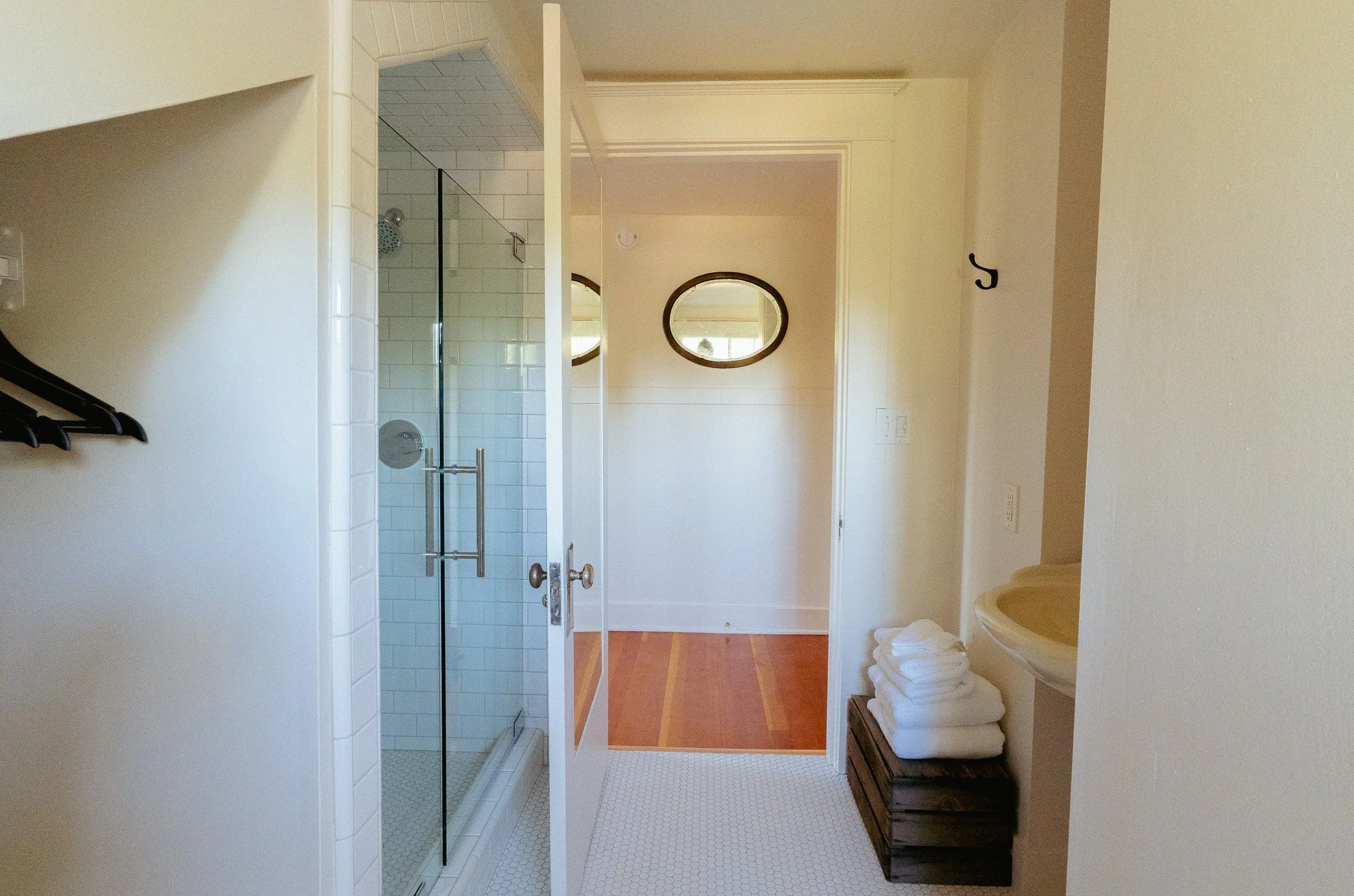 A bathroom with a walk-in shower with glass door, a wall mirror, and folded white towels on a dark wooden bench.