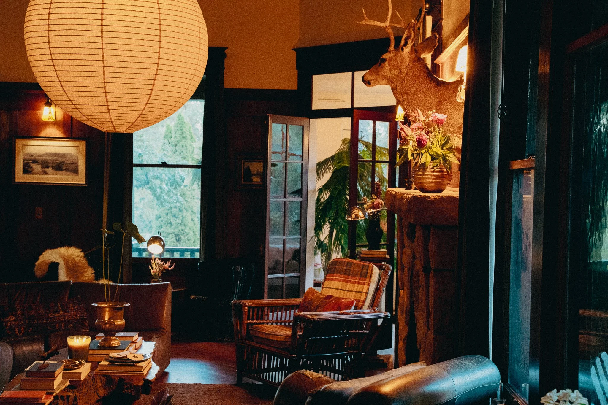 A cozy living room with warm lighting, a large paper lantern, a mounted deer head, a flower arrangement, and various decorative furniture and artworks.
