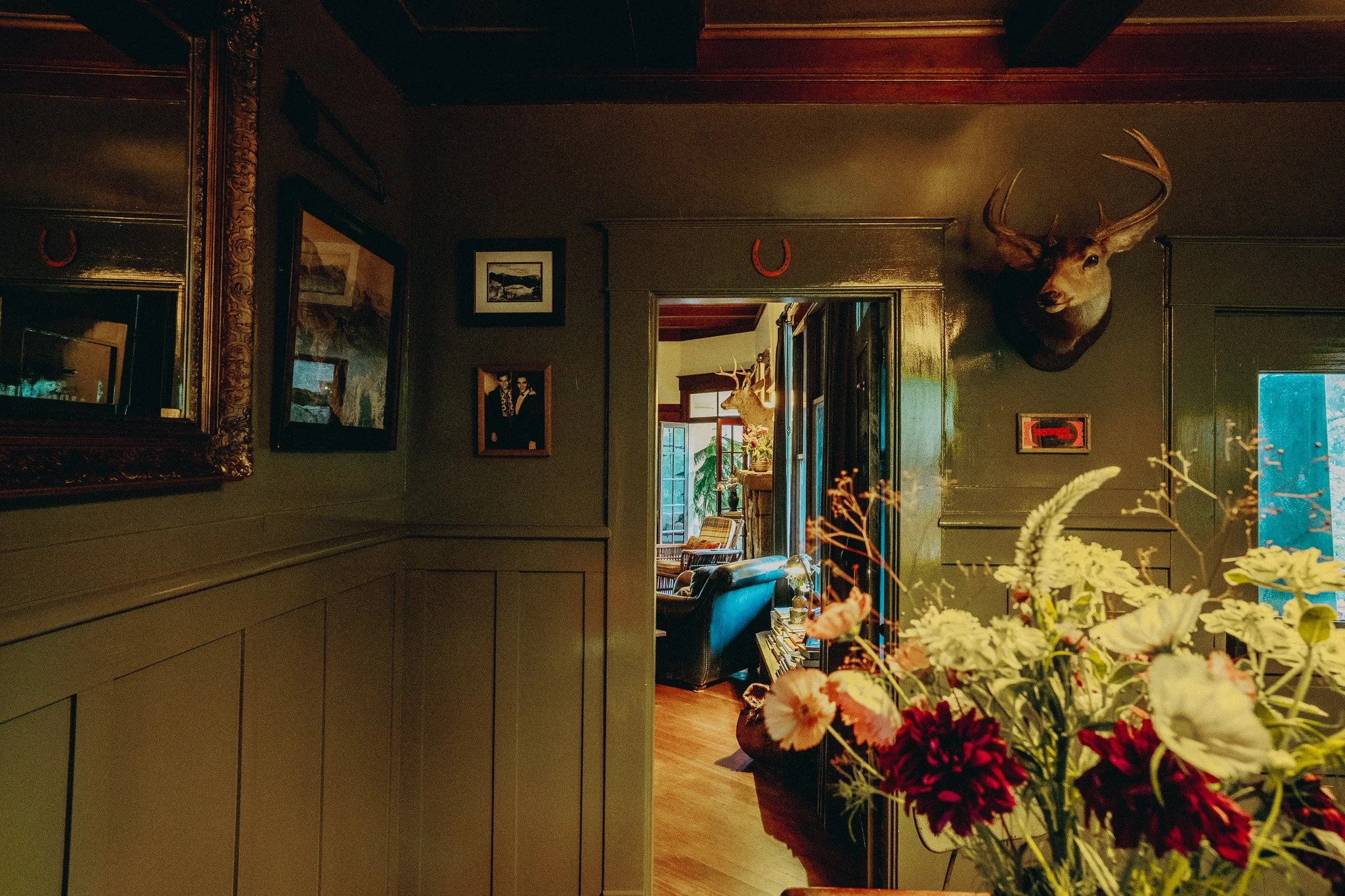 Interior of a cozy room with framed pictures on the walls, a mounted deer head, and a large bouquet of colorful flowers in the foreground.