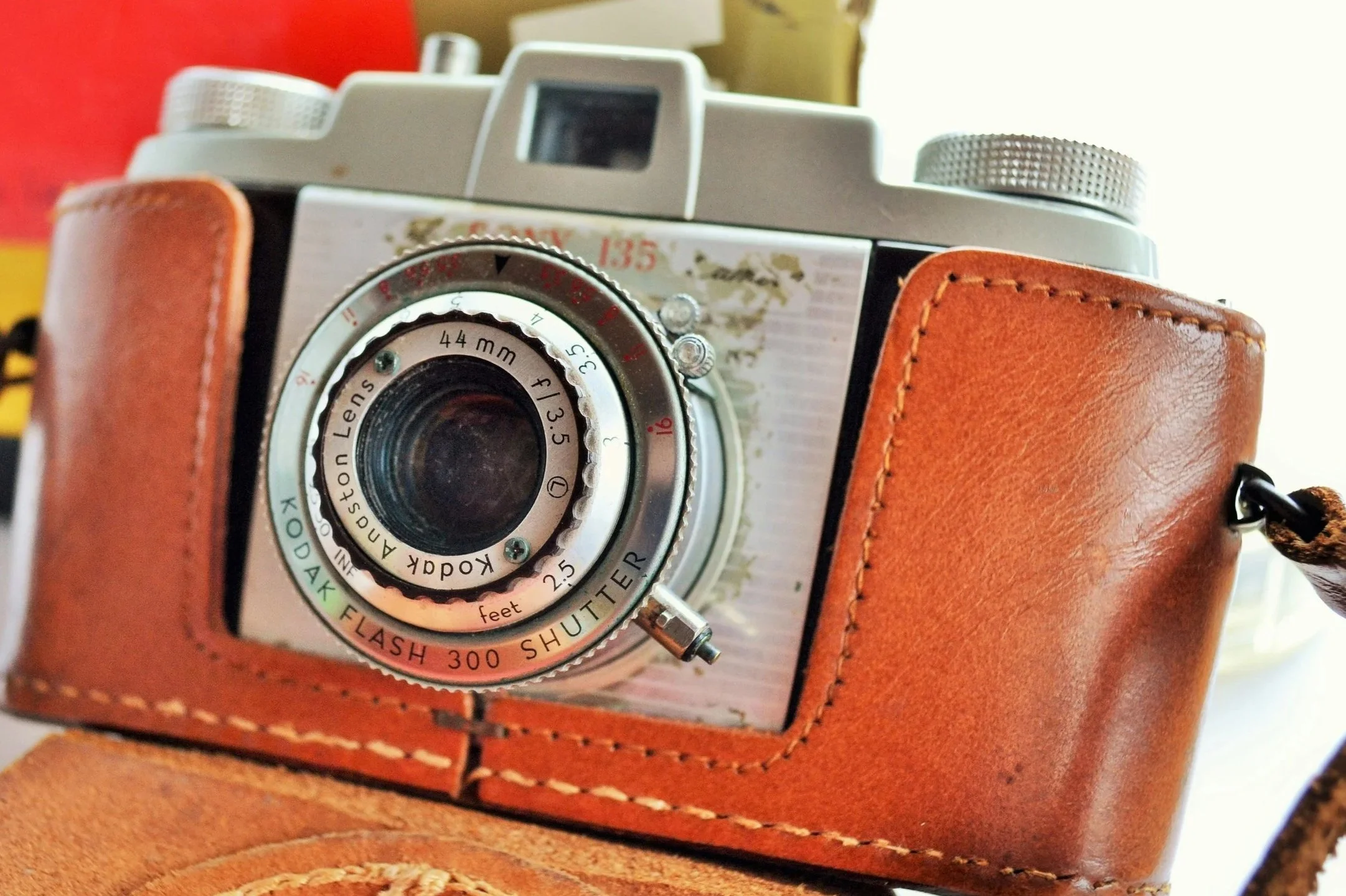 Close-up of a vintage camera with a leather case and metal dials, behind a glass lens, on a leather surface.