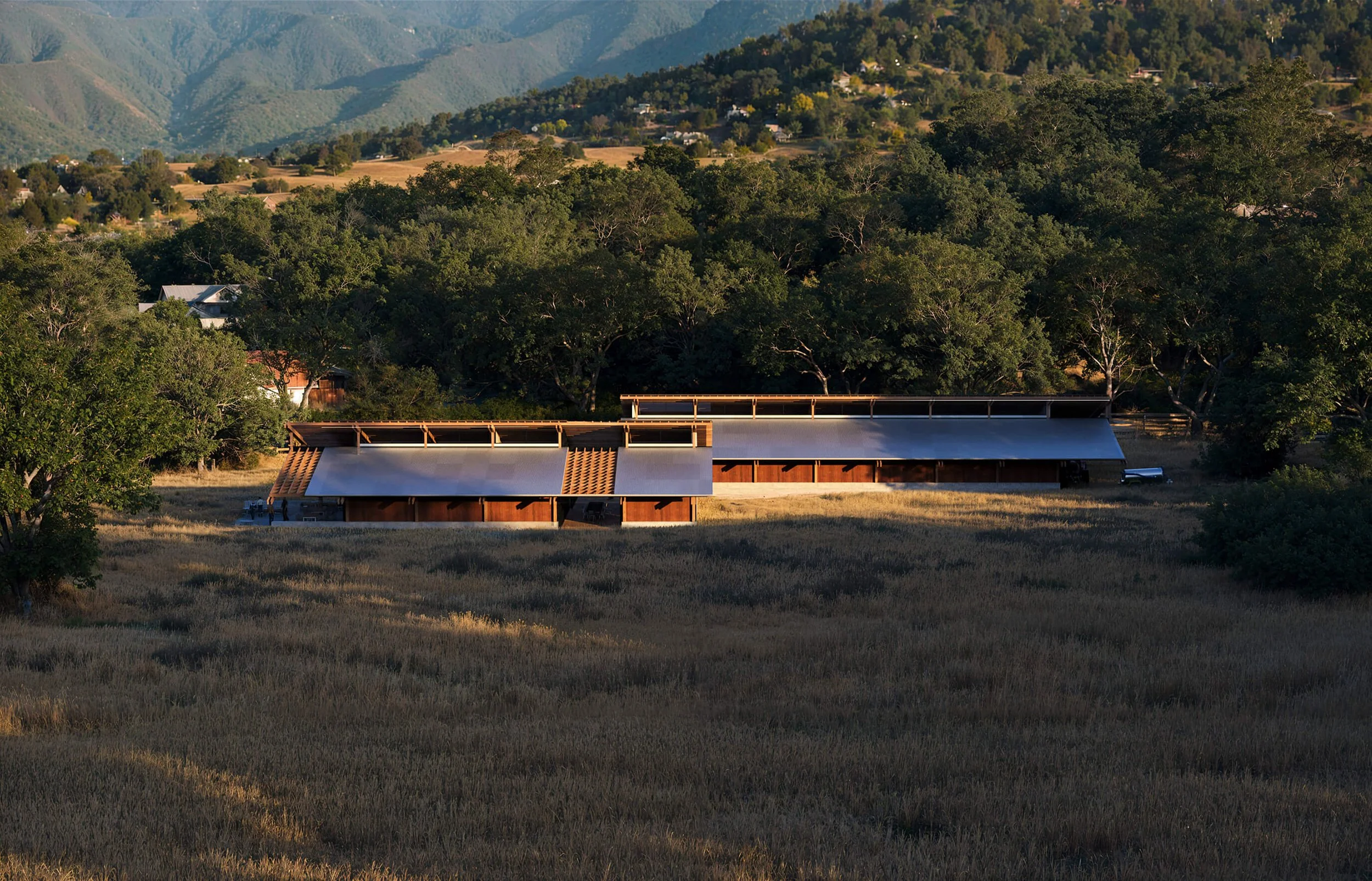 Long horizontal profile of SoCal Rancho settled into the surrounding meadow and hills