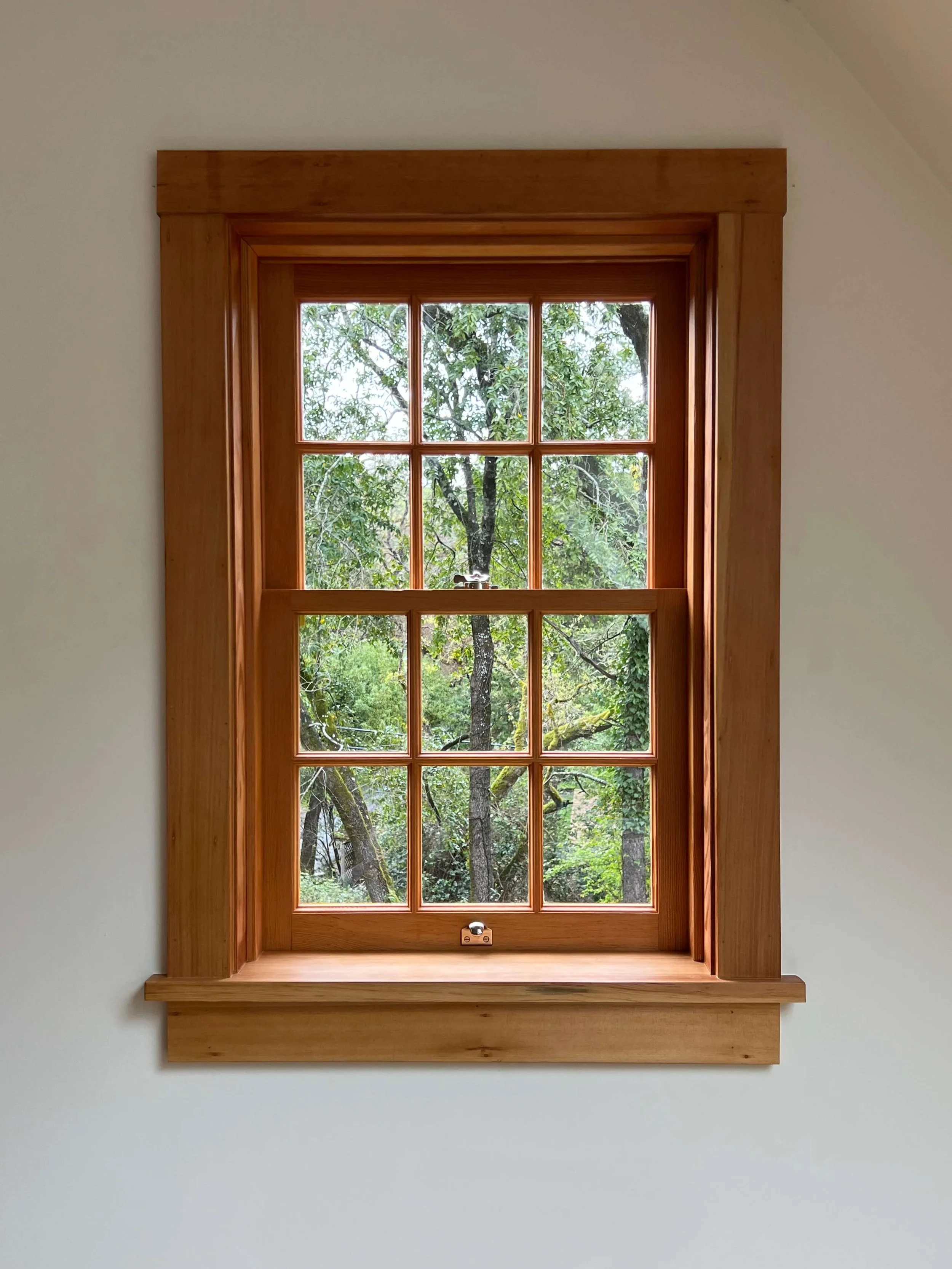Deeply trimmed wood sash window framing mature Oak trees at the restored Saltbox house