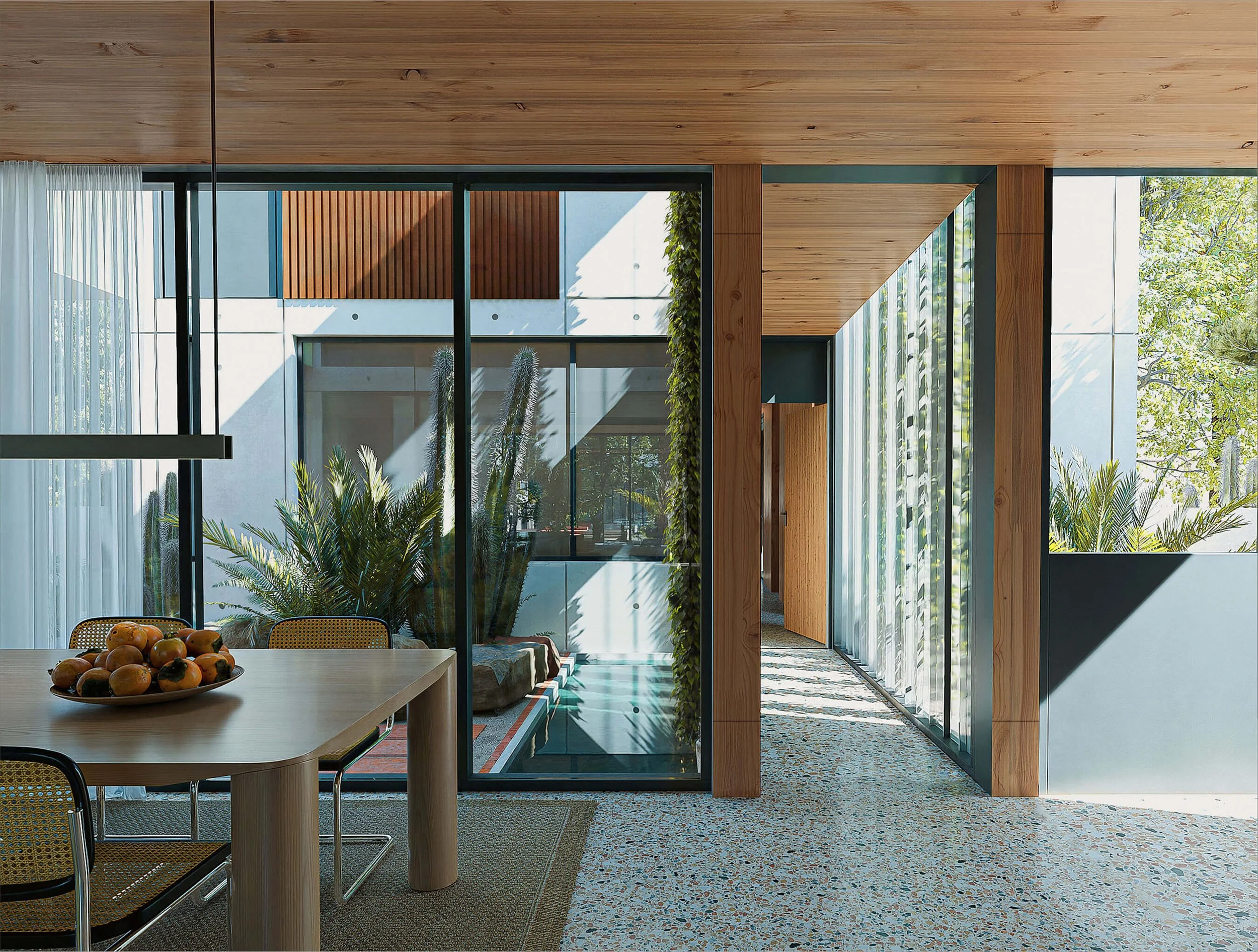 Dining room opening across glass walls to an internal courtyard at Dappled House