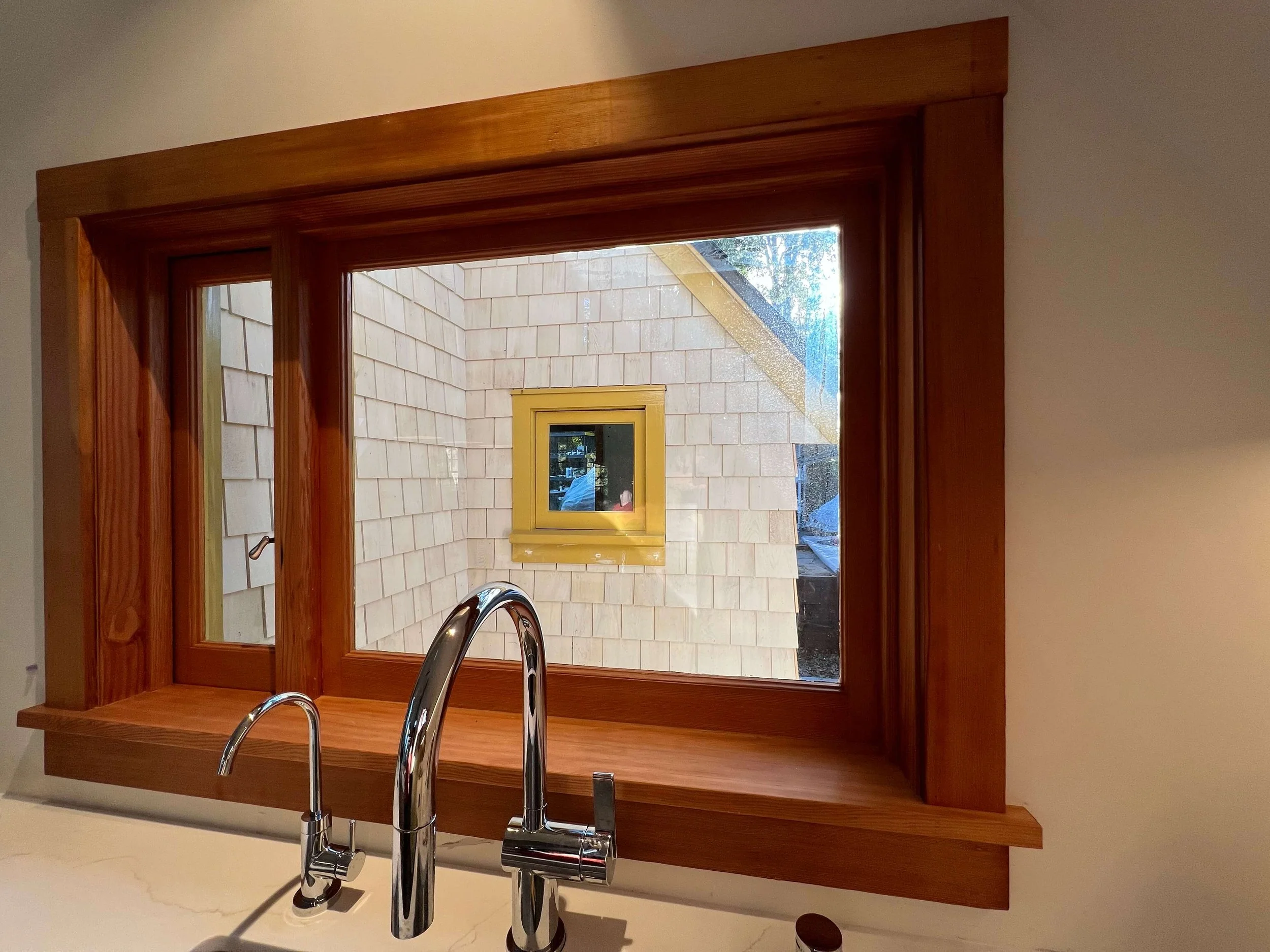 Wood-trimmed kitchen window framing the cedar-shingled exterior beyond