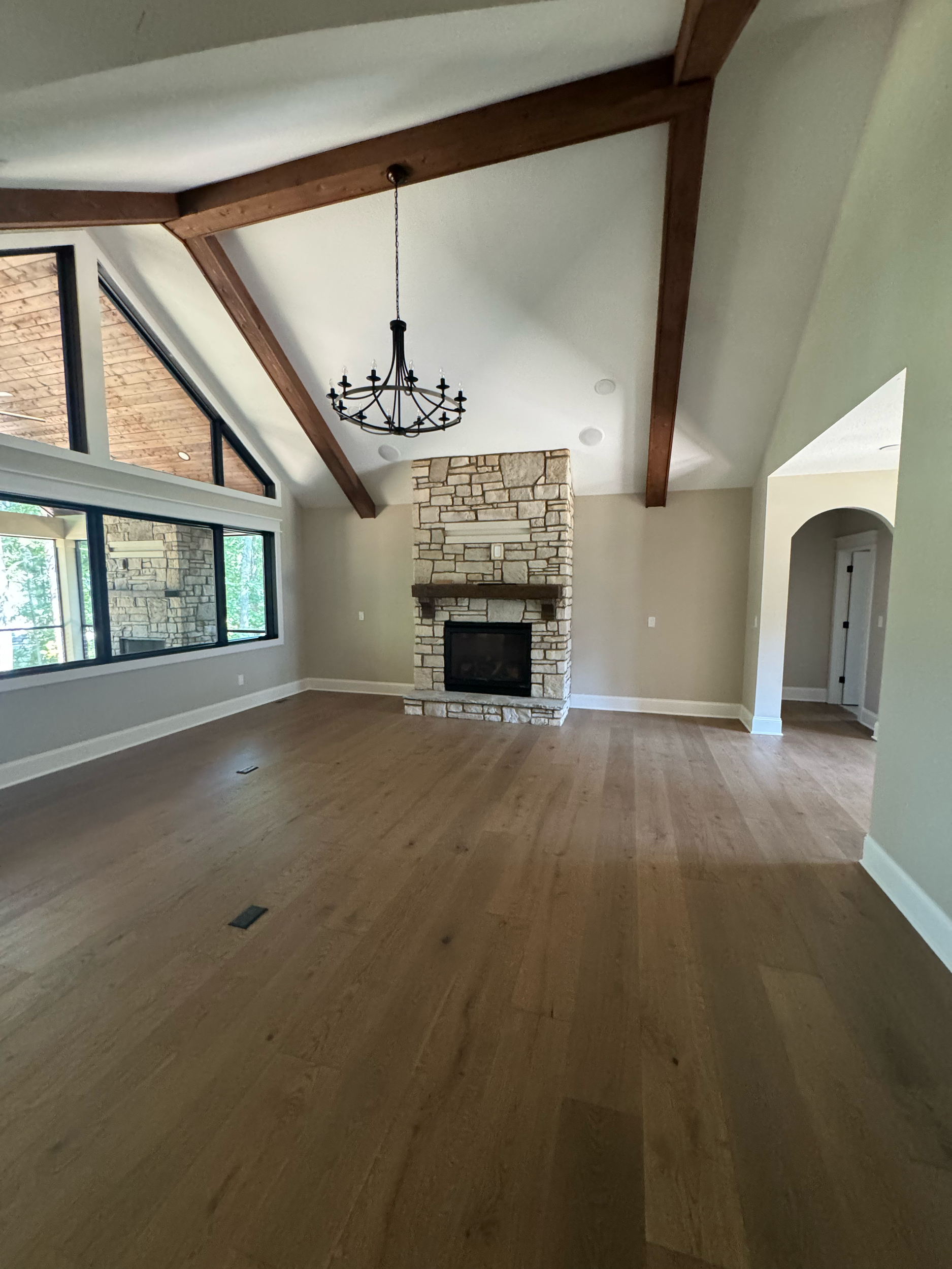 Living room with large windows, a fireplace with a stone surround, hardwood floors, and a chandelier hanging from the ceiling.