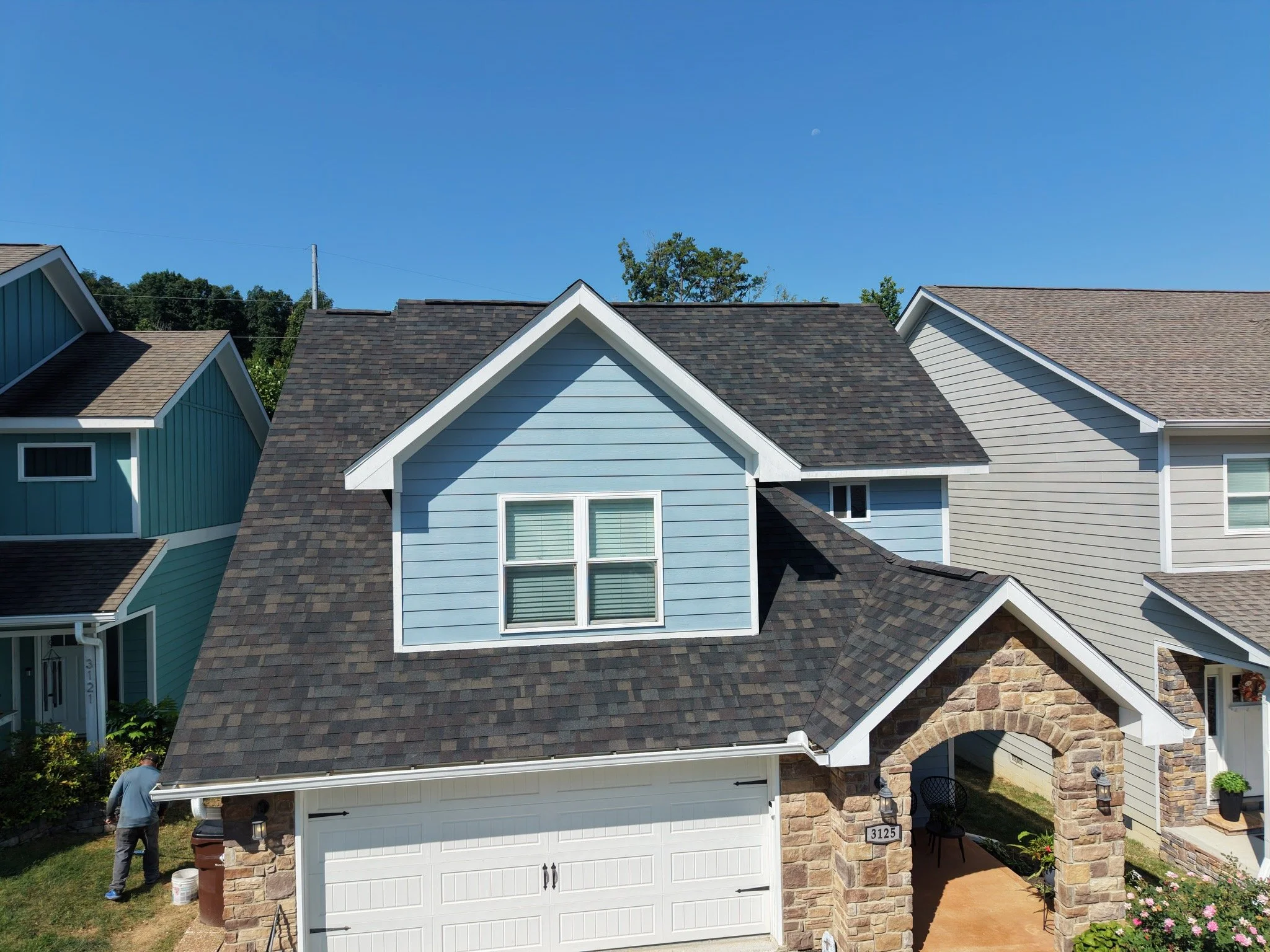 A row of houses with different colored exteriors, with a clear blue sky overhead, and a person walking near the front of one house.