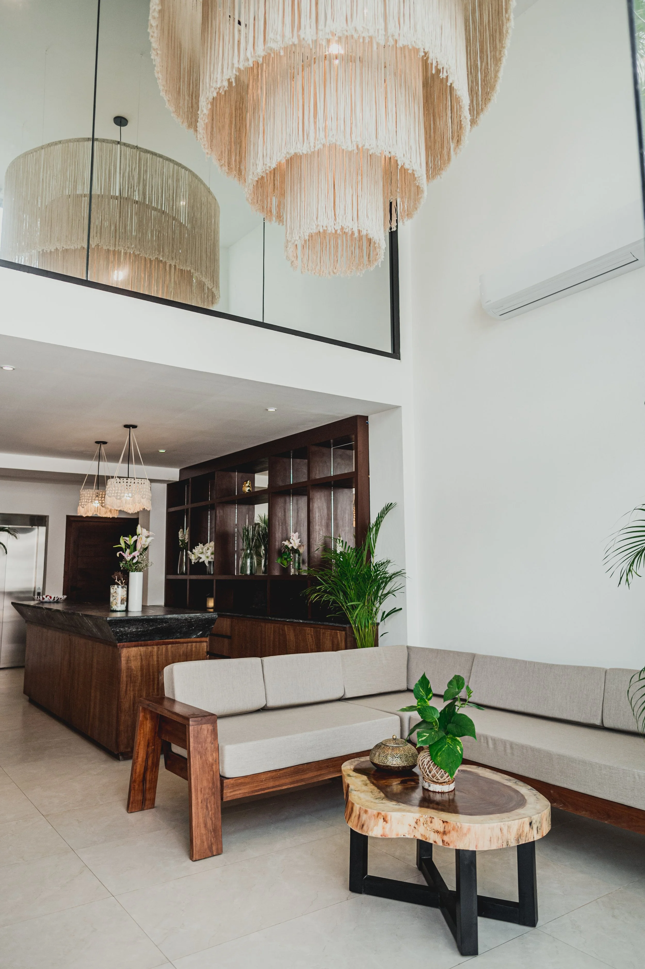 Sala moderna con muebles de madera, plantas y lámparas decorativas, vista desde el área de comedor hacia la sala.