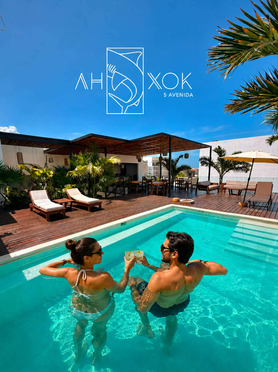 Dos personas en la piscina disfrutando y brindando con bebidas con rodajas de limón, rodeadas de palmeras, sillas y sombrillas en una terraza con cielo azul.