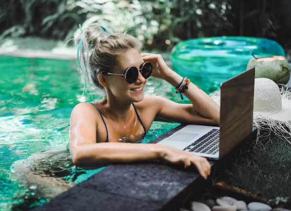 Mujer en la piscina usando gafas de sol y trabajando en una computadora portátil