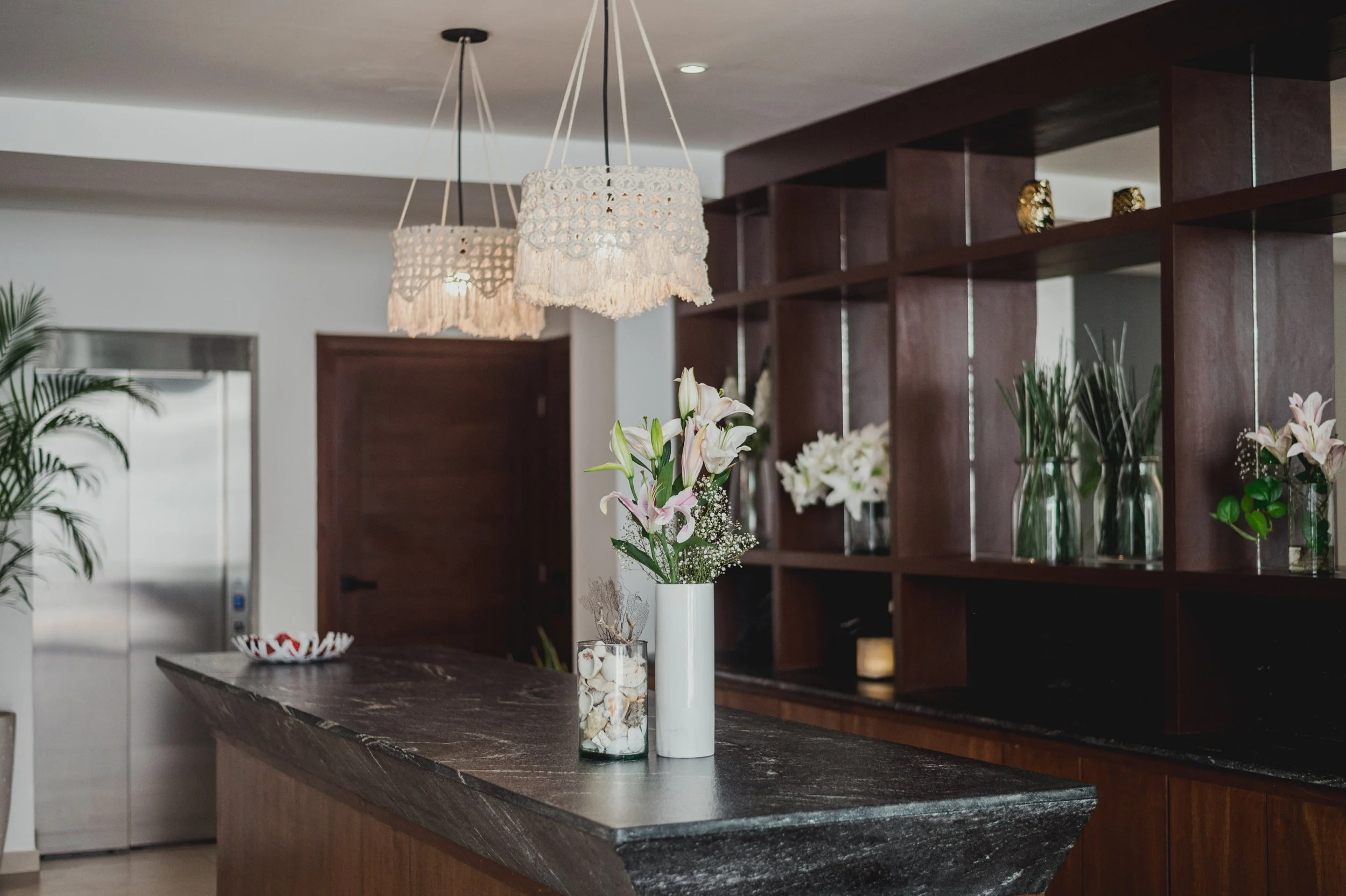 Interior de una sala con mesas decoradas con flores en jarrones y lámparas colgantes de estilo bohemio.