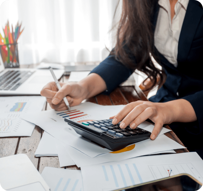 Person working at desk, using a calculator, surrounded by papers and charts.