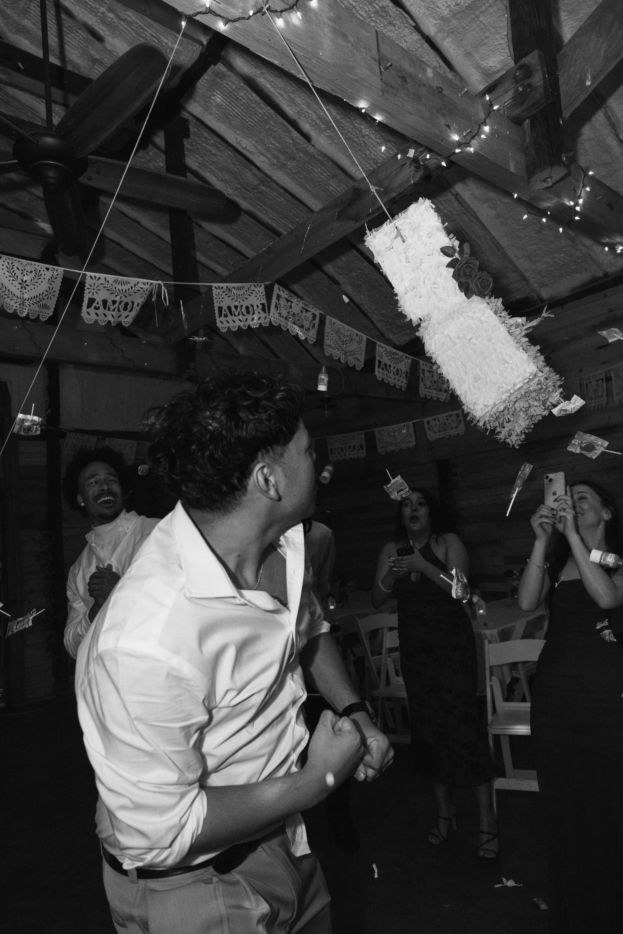 People celebrating at a party with decorations, a piñata hanging from the ceiling, and festive string lights.