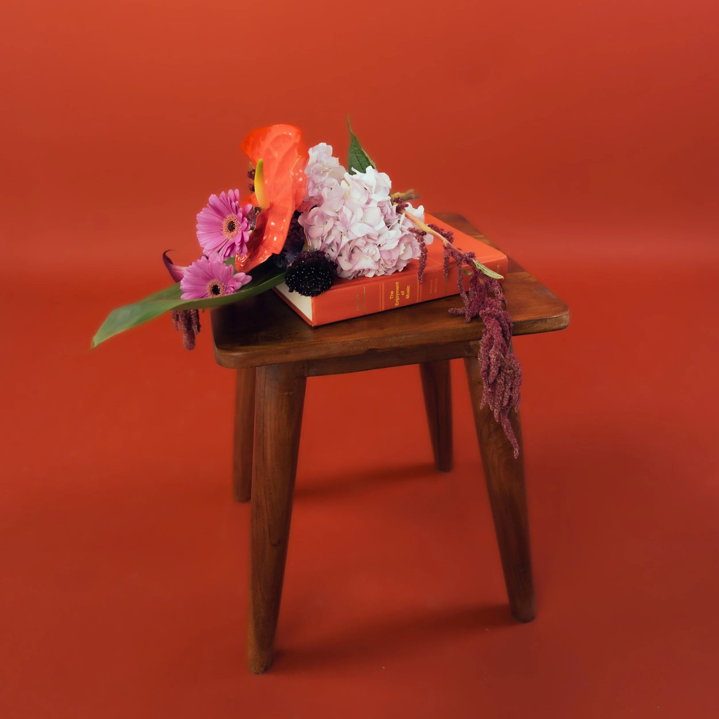 A still life arrangement of various flowers on a wooden table against an orange background, positioned atop an orange book.