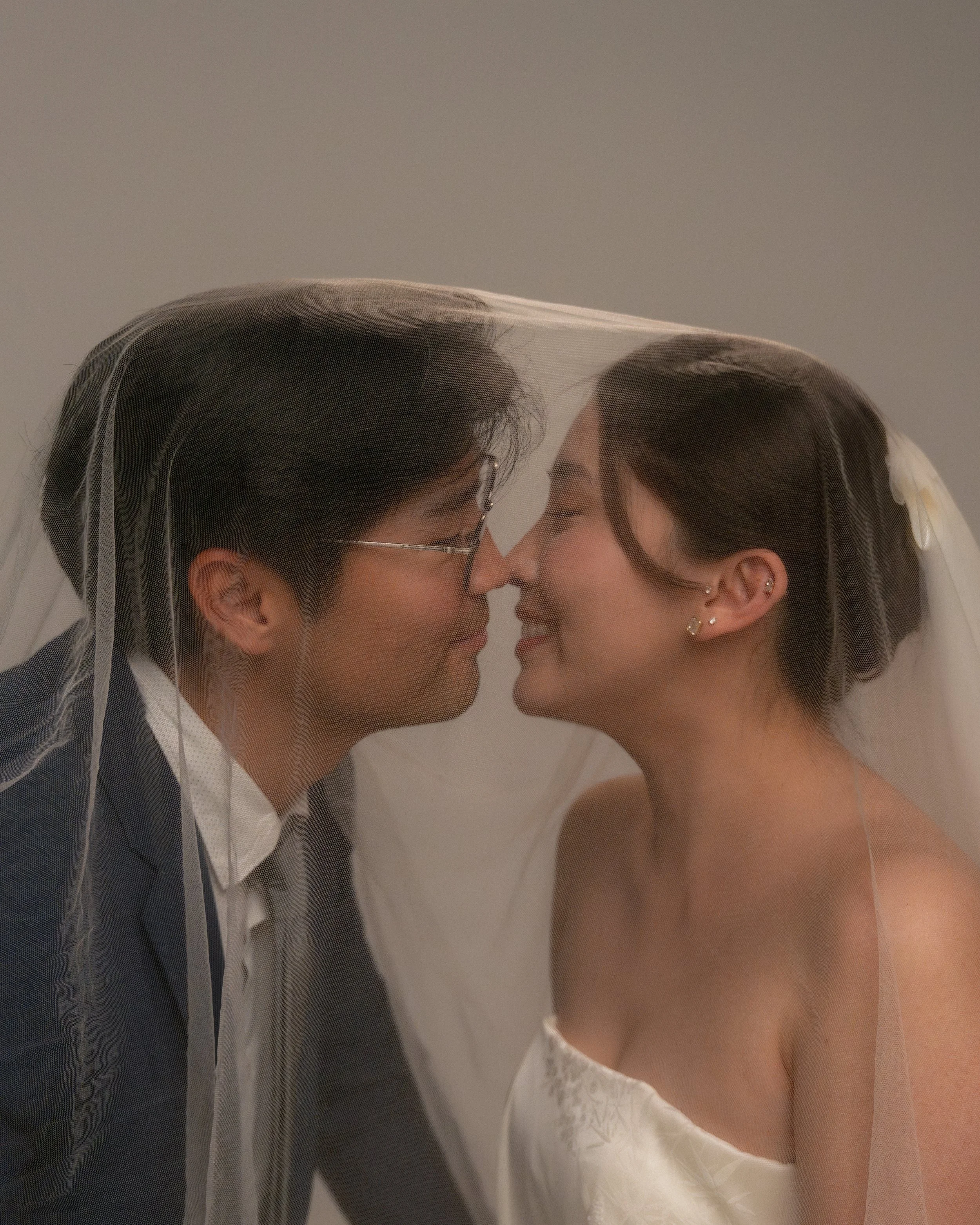 A groom and bride face to face, wearing a veil, close-up shot of their faces touching.