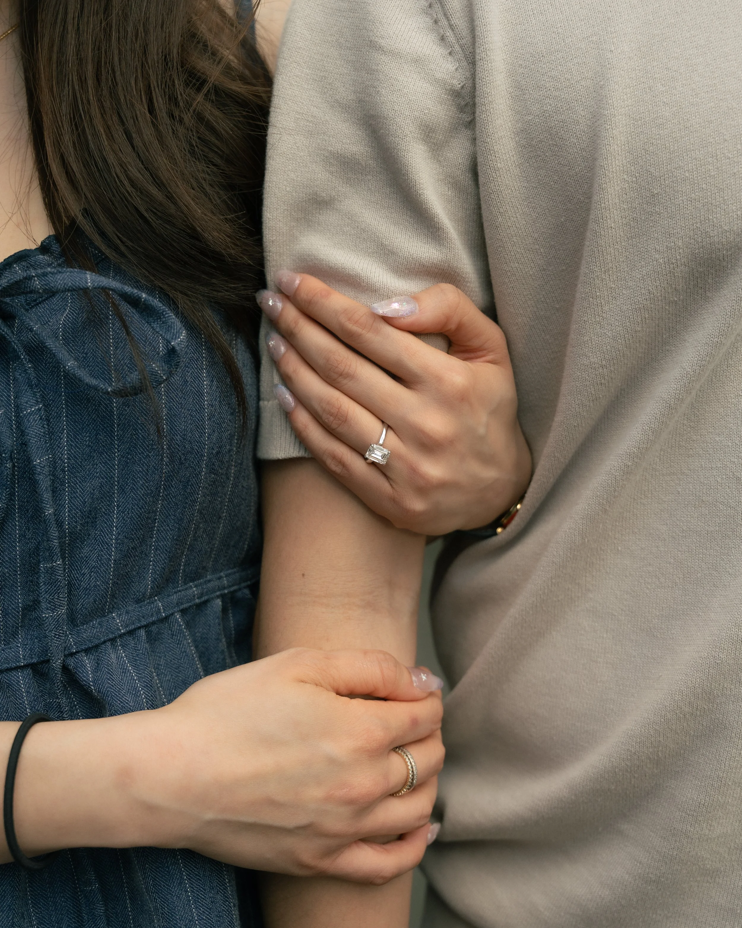 Close-up of two people embracing, with one person wearing a beige sweater and the other wearing a dark plaid shirt, showing their hands gently holding each other's arms.