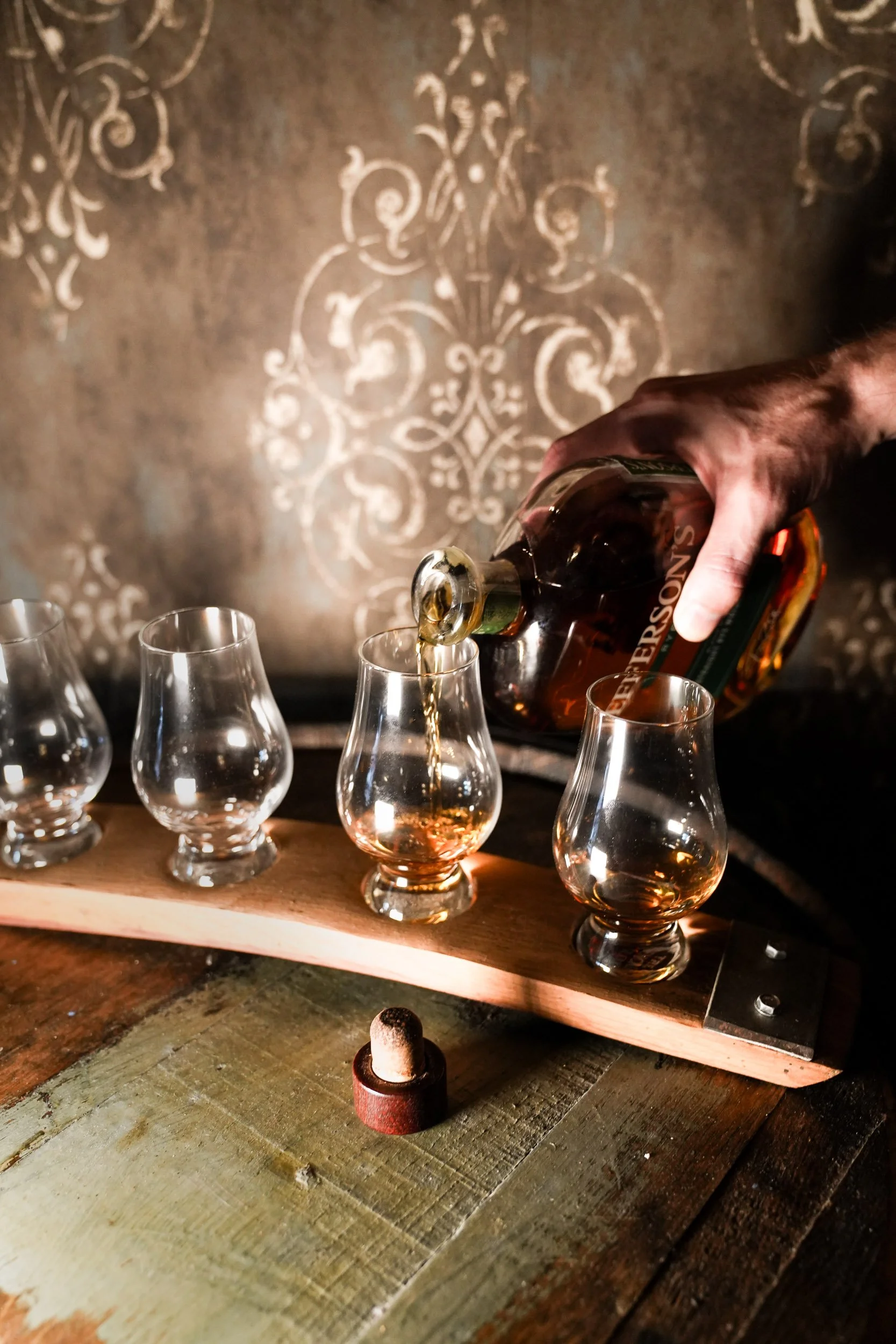 A flight of whiskey being poured on top of an aged barrell.