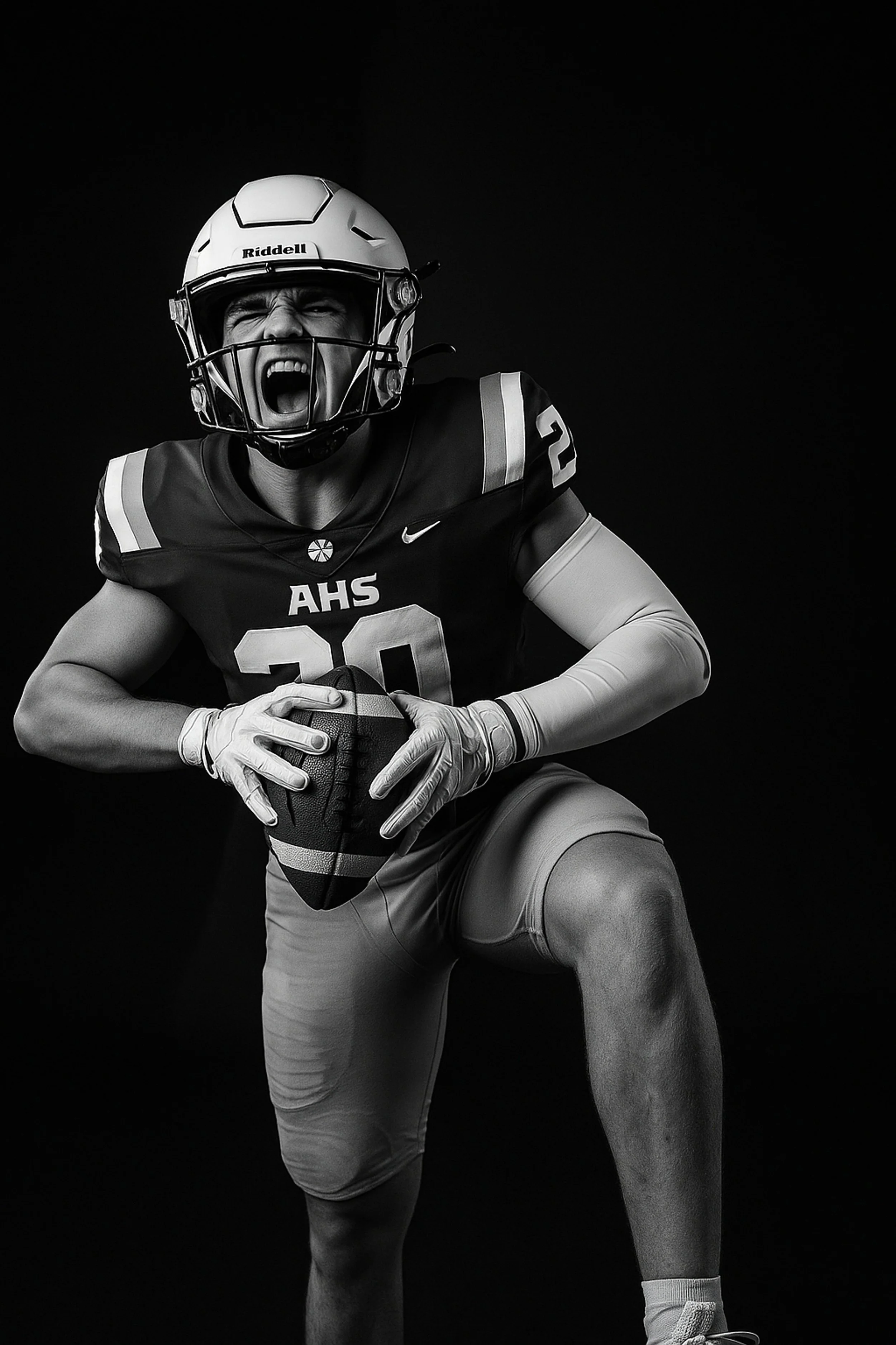 Black and white photo of a football player in a helmet and uniform holding a football, with a dark background, shouting or celebrating.