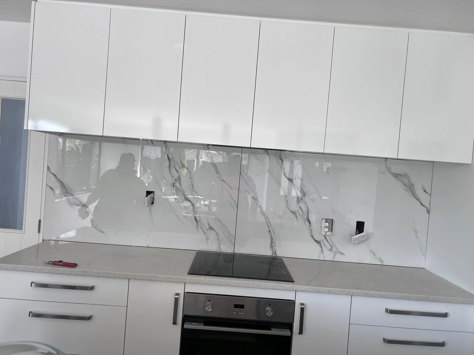 Modern kitchen with white cabinets, gray countertop, marble backsplash, and built-in oven.