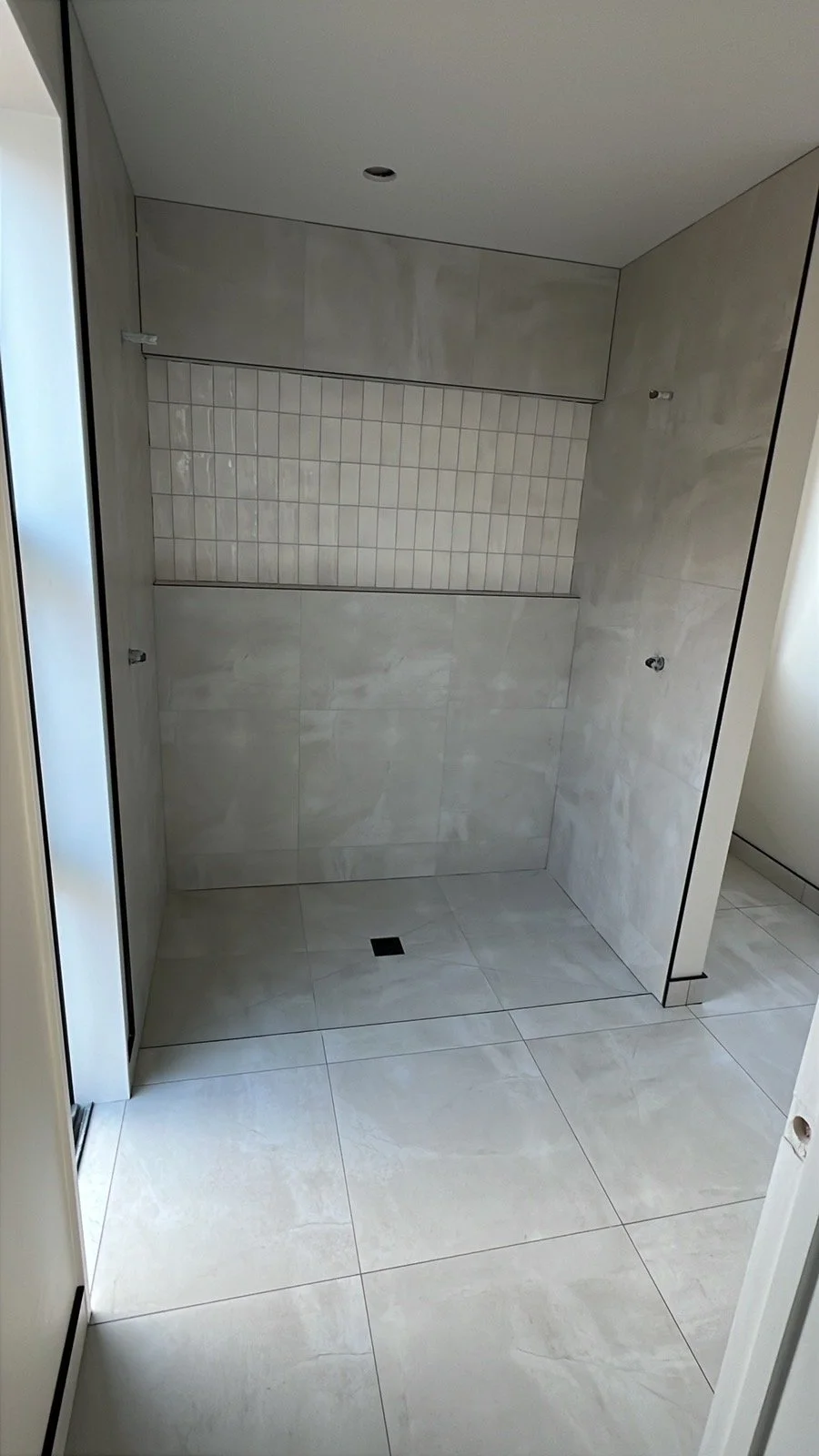 Empty bathroom shower area with tiled walls and floor, and a drain in the center of the floor.