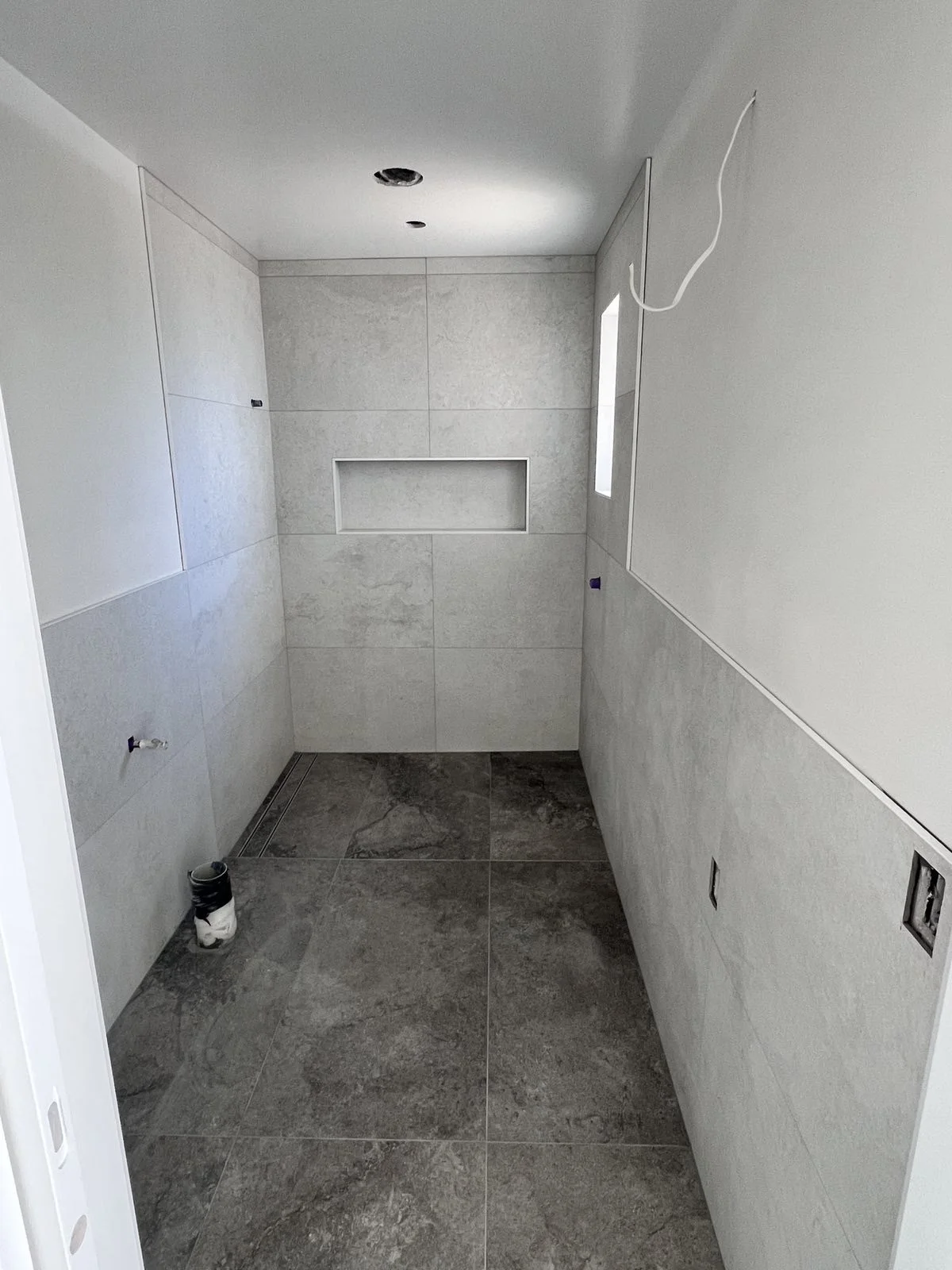 Bathroom in progress with tiled walls and floor, electrical wiring, and plumbing fixtures yet to be installed.