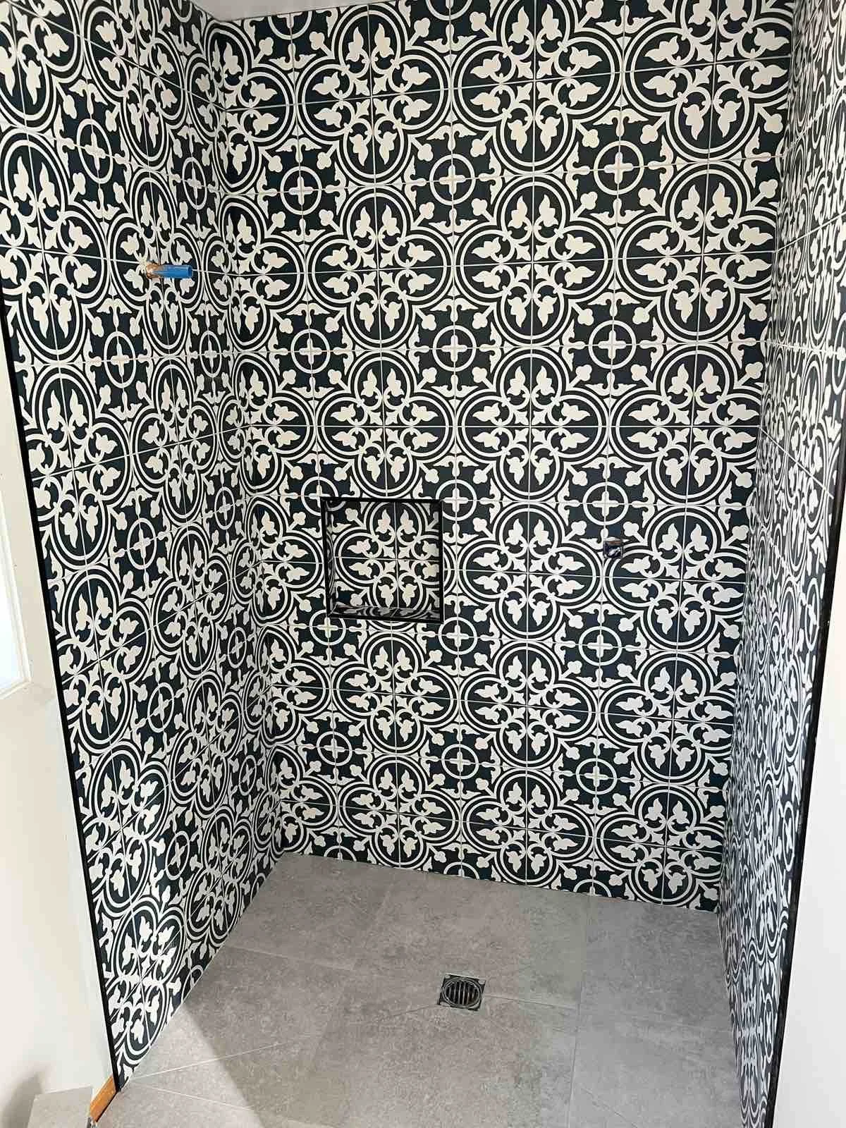 A shower area with black and white patterned tiles on the walls, a small built-in tile shelf, and a drain on the floor.