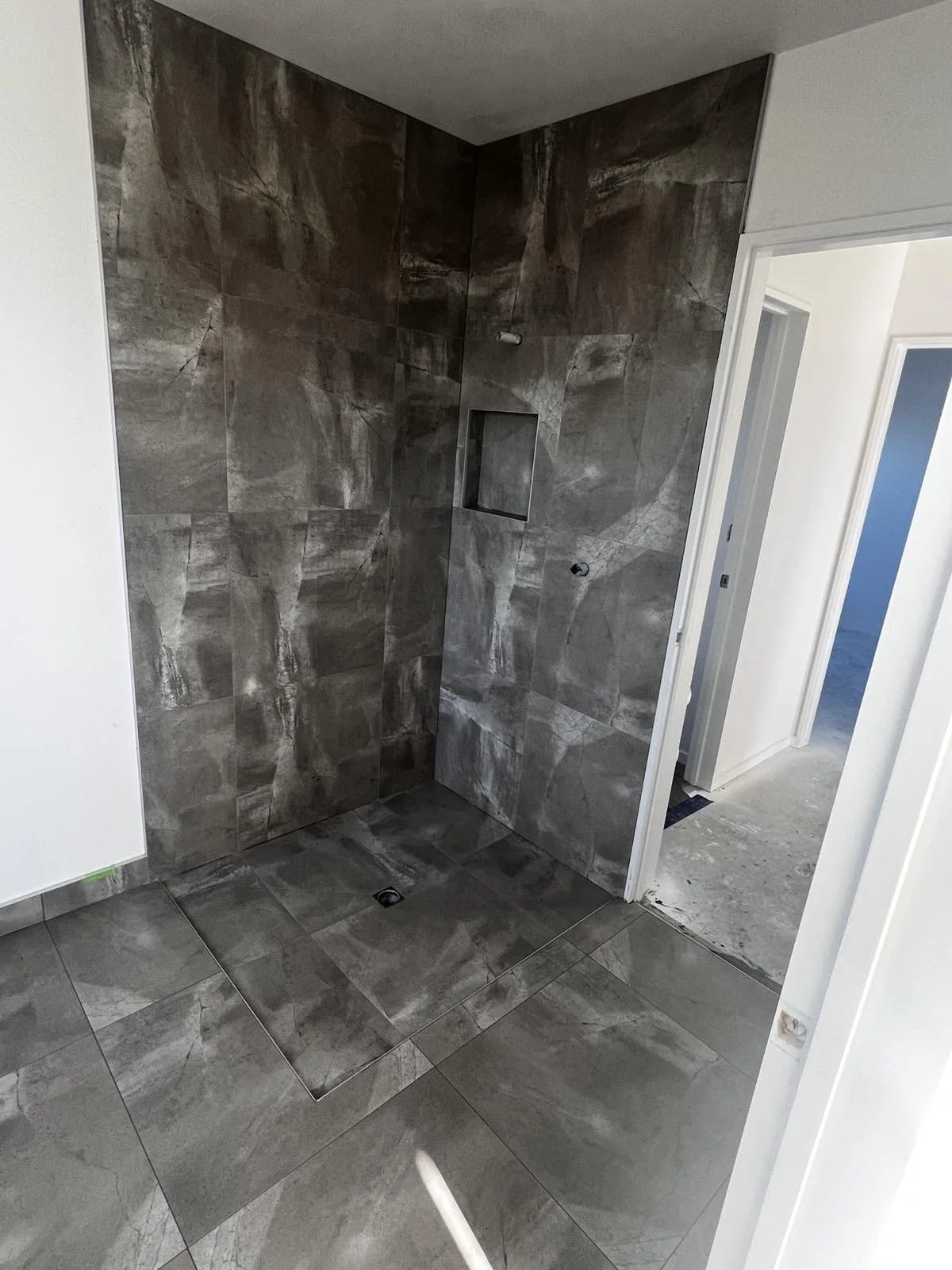 Bathroom with dark gray marble tiles on walls and floor, large walk-in shower with built-in niche, and a door leading to another room.