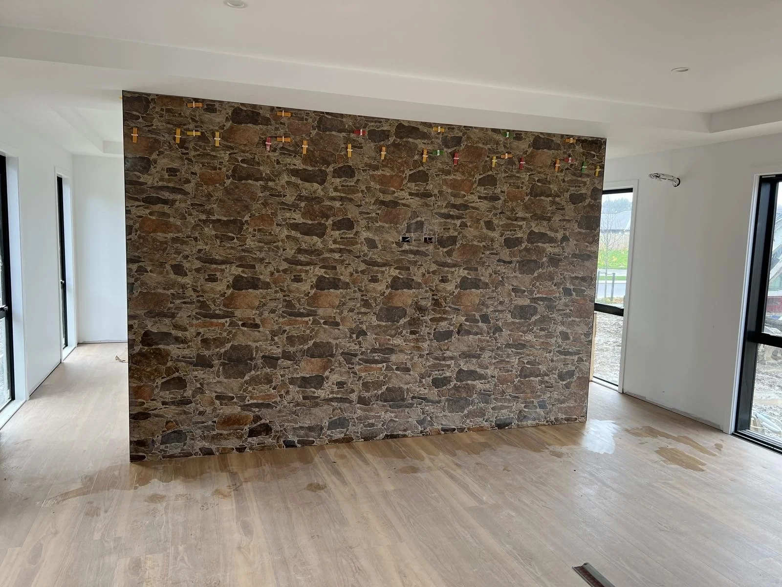 Unfinished interior room with a stone accent wall, wood flooring, and large windows and sliding glass doors showing an outdoor landscape.