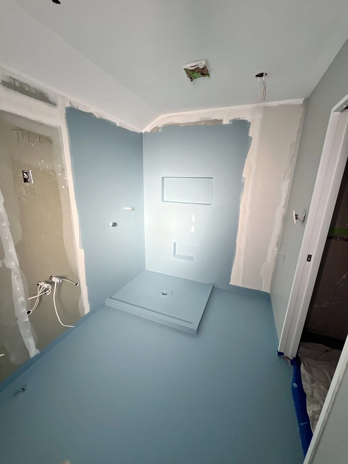 Bathroom under construction with a blue shower base, light blue walls, and unfinished wall areas with visible drywall and electrical wiring.