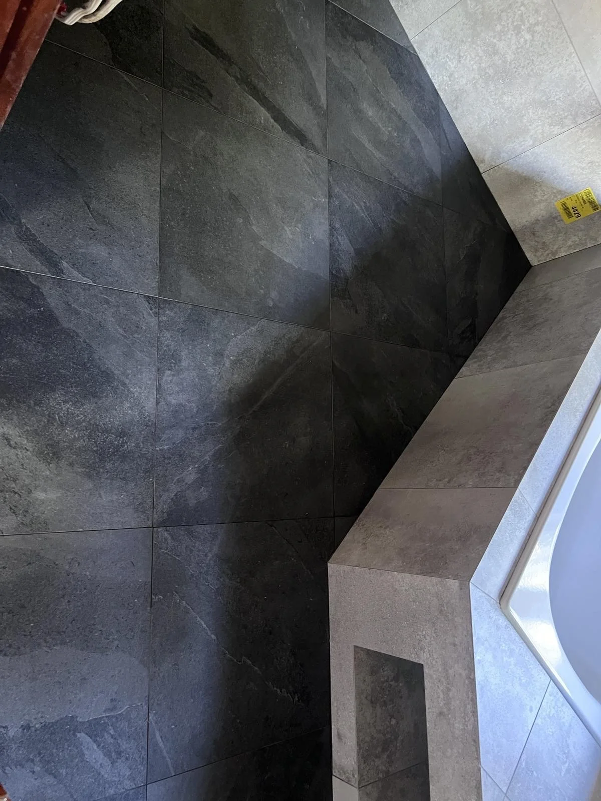 Dark gray tiled floor and a beige tiled step or platform near a window, with a yellow price tag visible on the beige tiles.