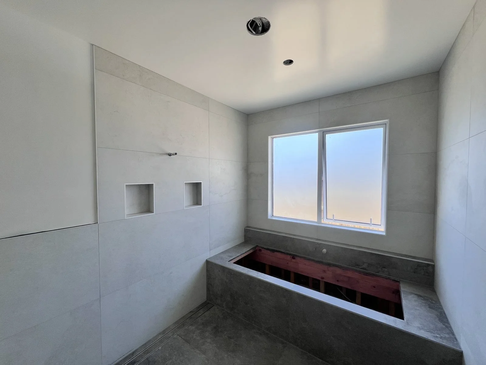 Bathroom under construction with a large window, tiled walls, and a built-in bathtub frame with red support beams.