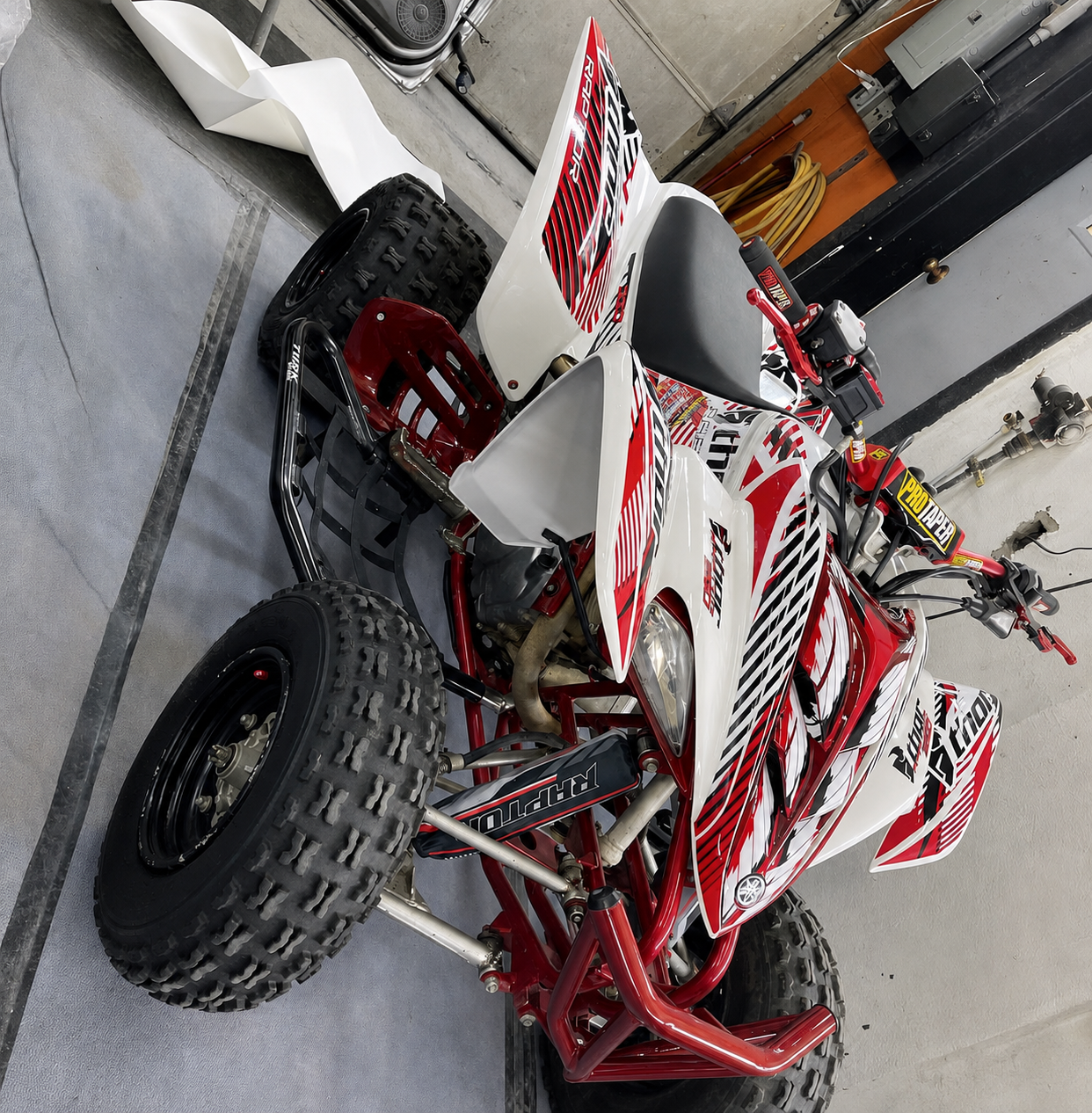 Red and white Yamaha YFZ450R all-terrain vehicle with black tires, parked indoors next to tools and equipment.