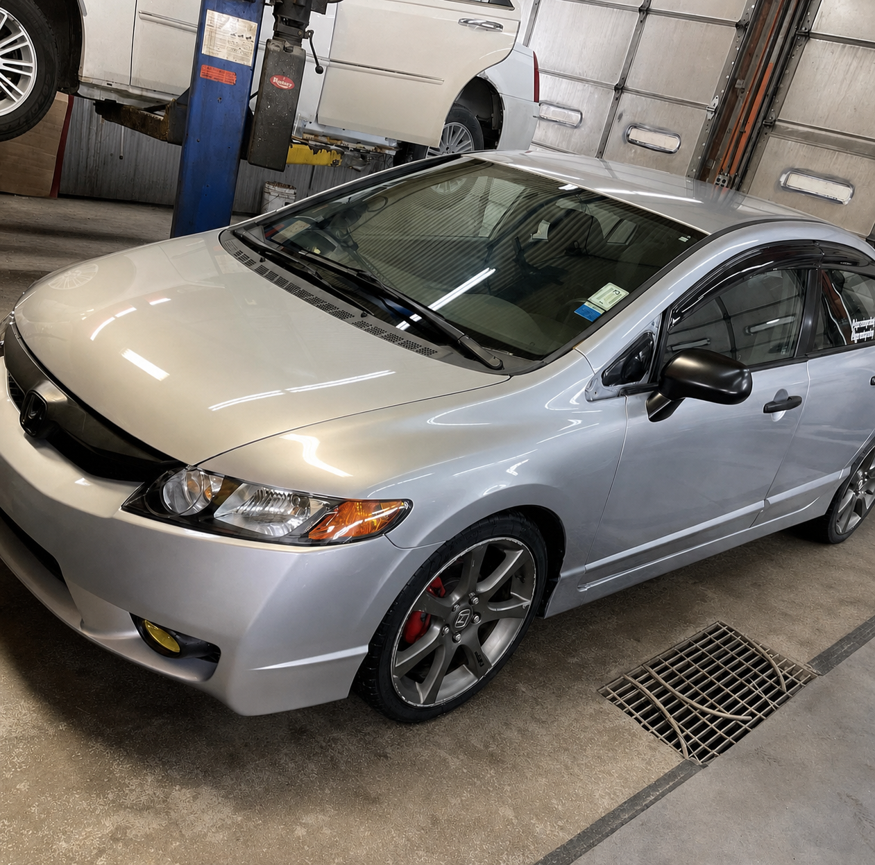 Silver Honda Civic parked inside a garage or workshop with a blue car lift in the background.