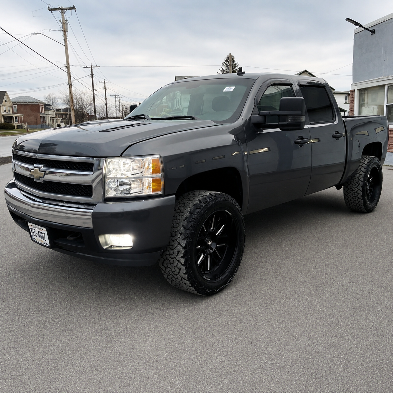 A black Chevrolet pickup truck parked on a street in a residential area with houses and utility poles in the background.