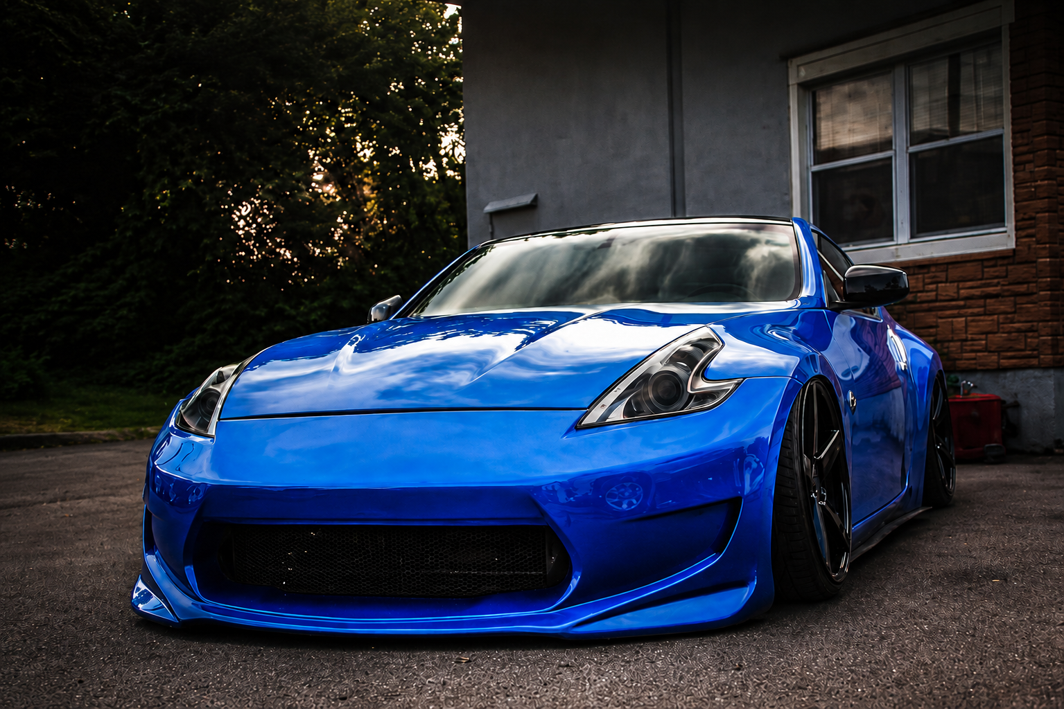 A sleek, blue sports car parked outside a residential building with trees and windows in the background.