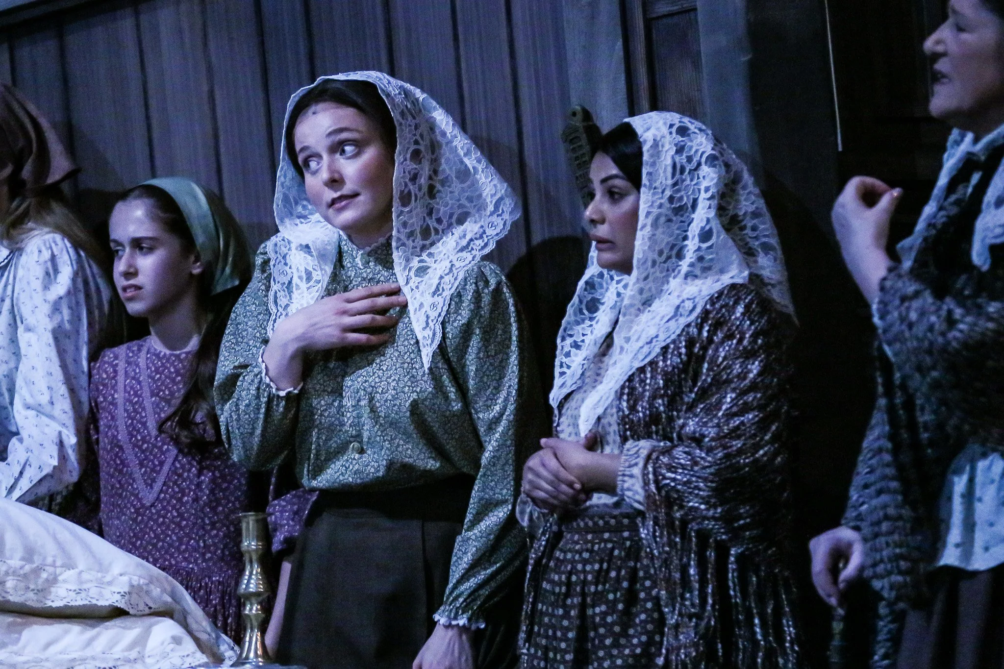 A group of women dressed in traditional clothing and lace head coverings, gathered in a room with wood-paneled walls, possibly attending a religious or cultural ceremony.