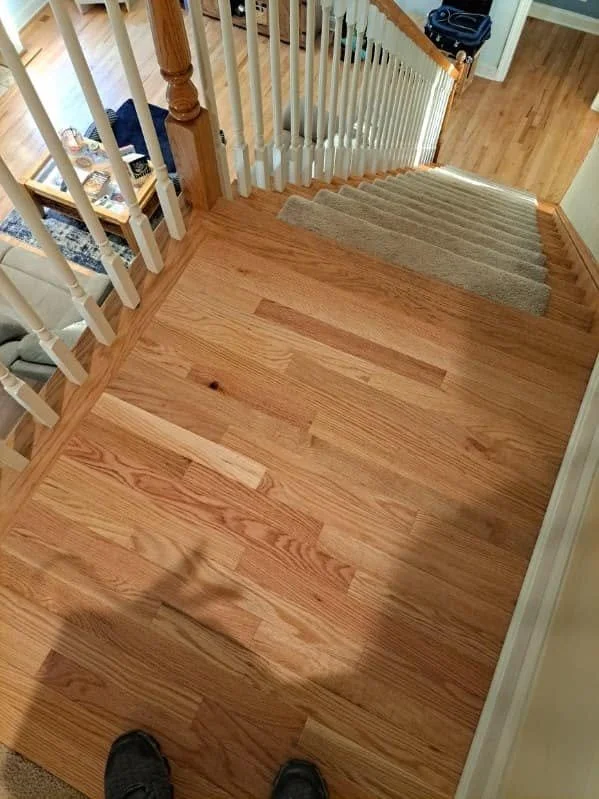 A view of a hardwood staircase and floor area, with a stair runner on the stairs, white spindles and wooden handrails, and a small table with items on it nearby.