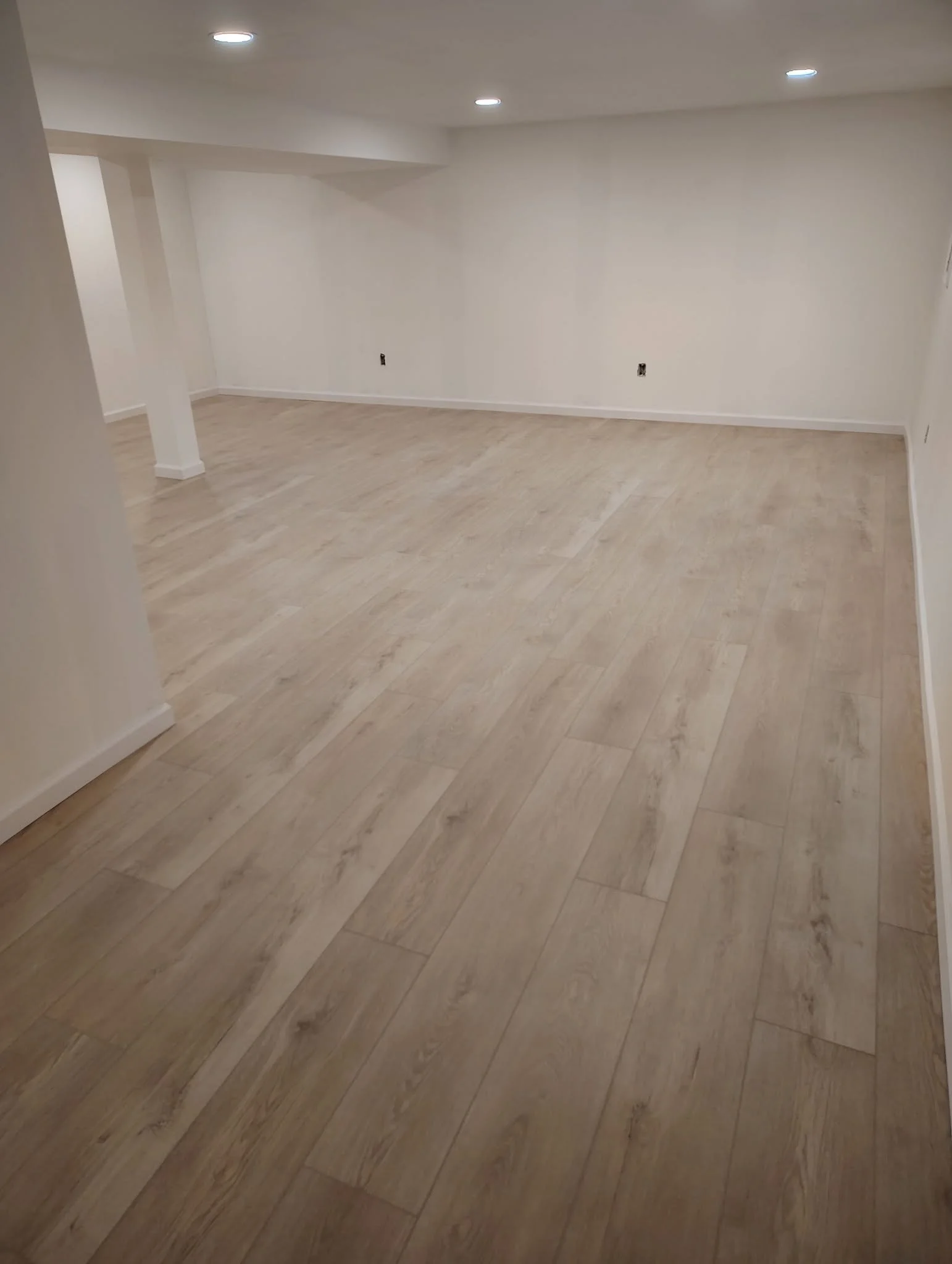 Empty modern living room with wood flooring, white walls, recessed lighting, and no furniture.