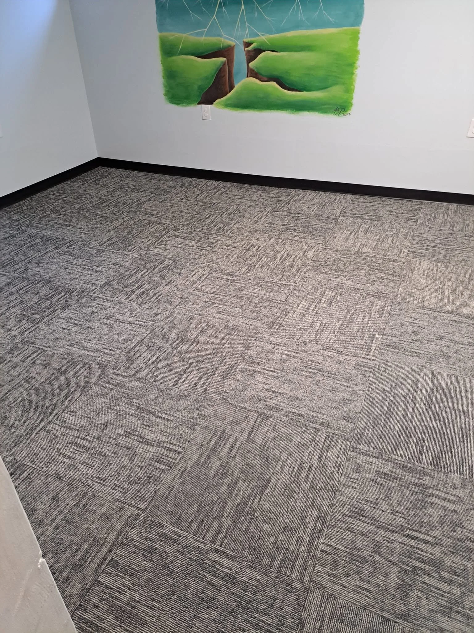 A corner of a room with a multicolored carpet and a wall painting featuring green hills, blue sky, and lightning.