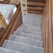 A staircase with gray carpeted steps and wooden side panels, leading downward.