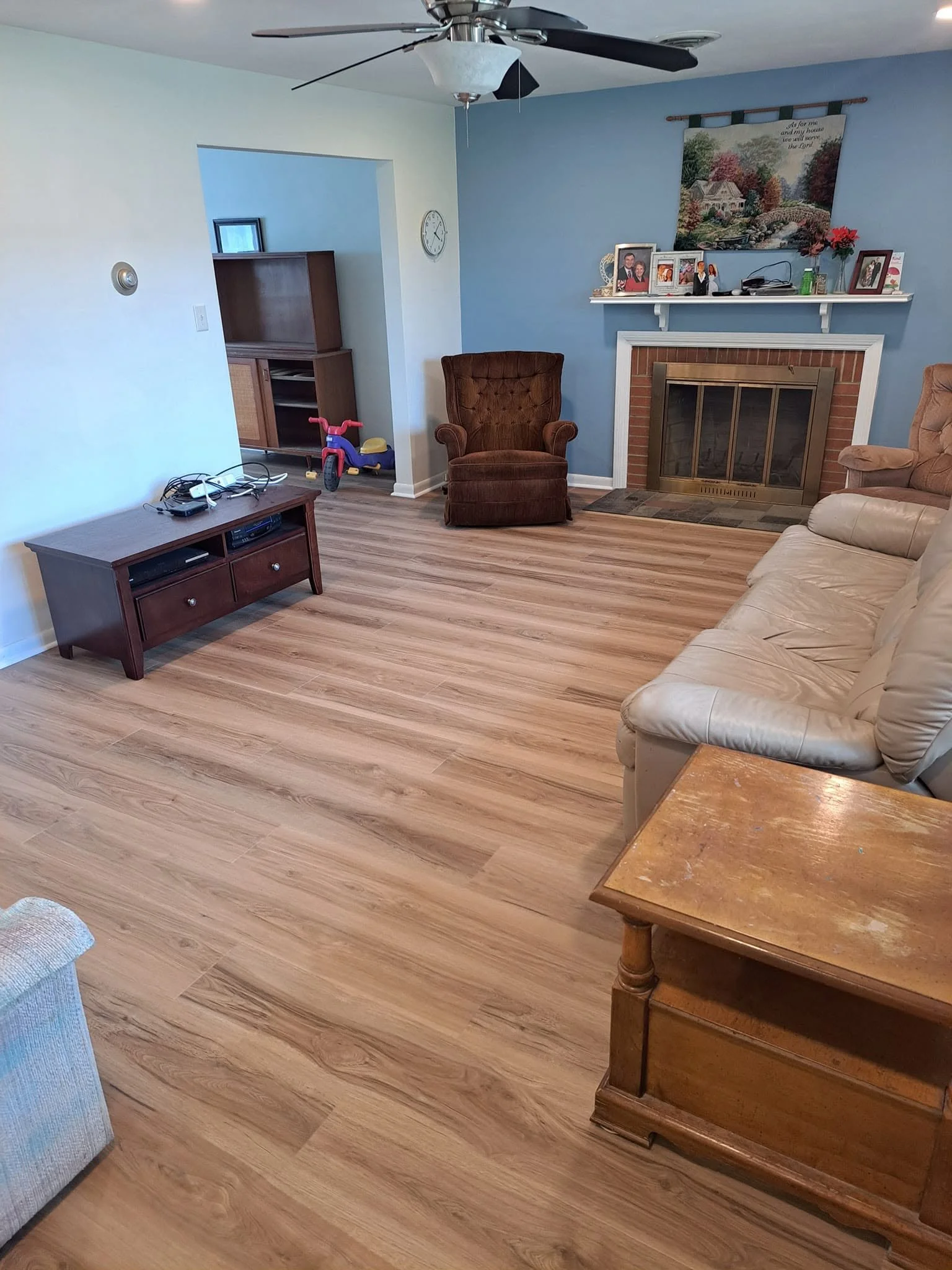Living room with beige and brown furniture, a blue wall with a fireplace, and a white shelf with family photos and decorations.