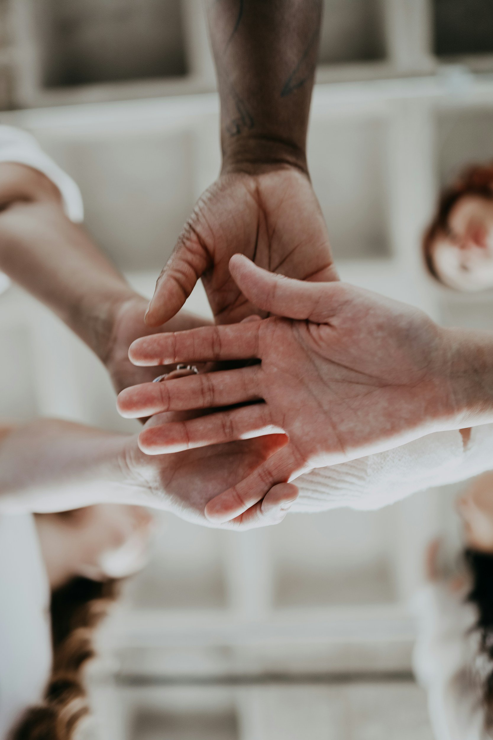 Multiple hands holding each other in a support gesture with a blurred background.